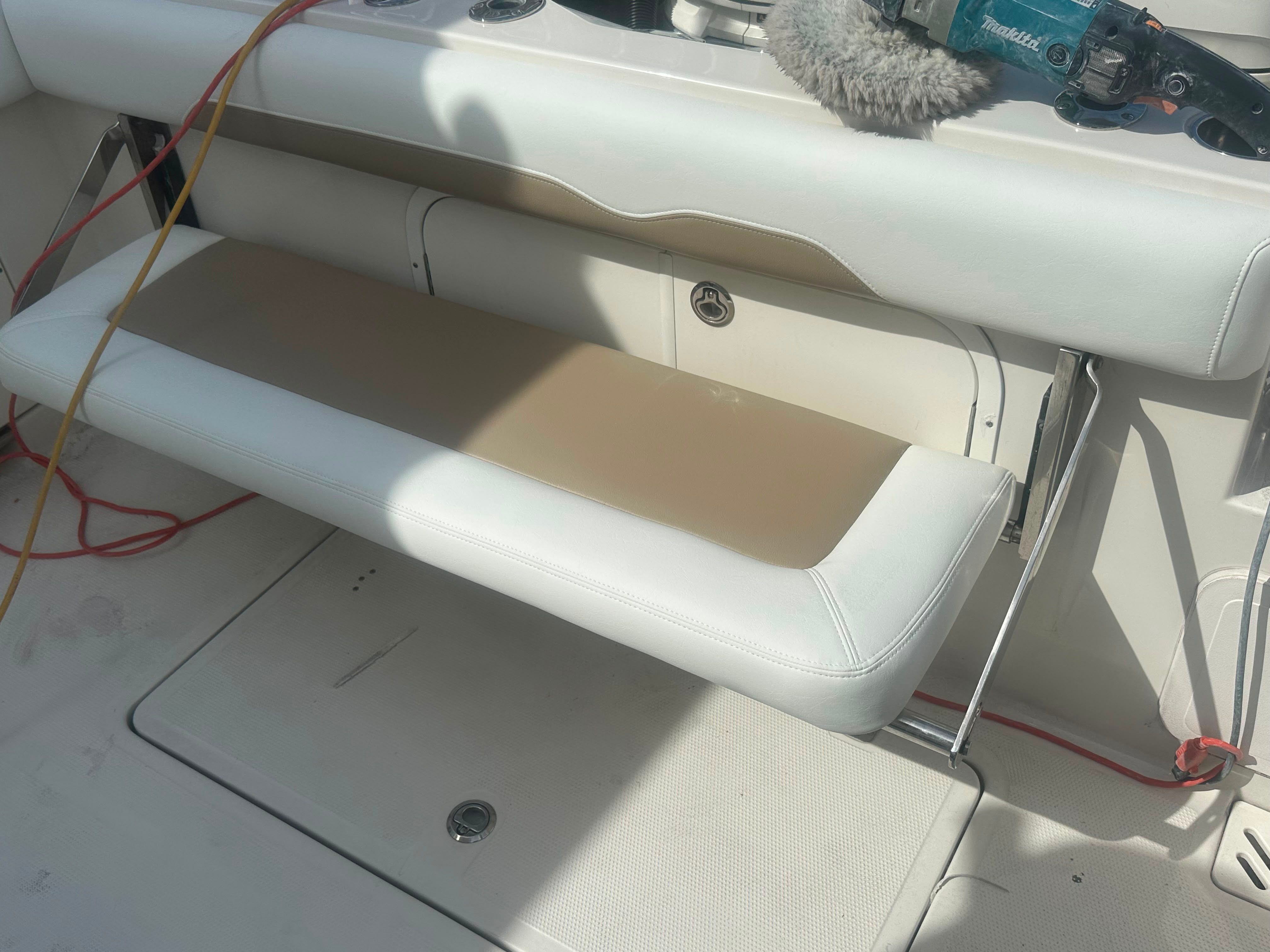 A white bench seat on a boat with cleaning tools and cables in the background.