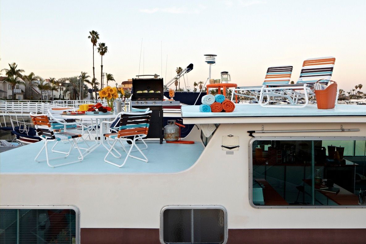 A 1975 Harbor Master houseboat with a rooftop deck, sun loungers, grill, and table with chairs.