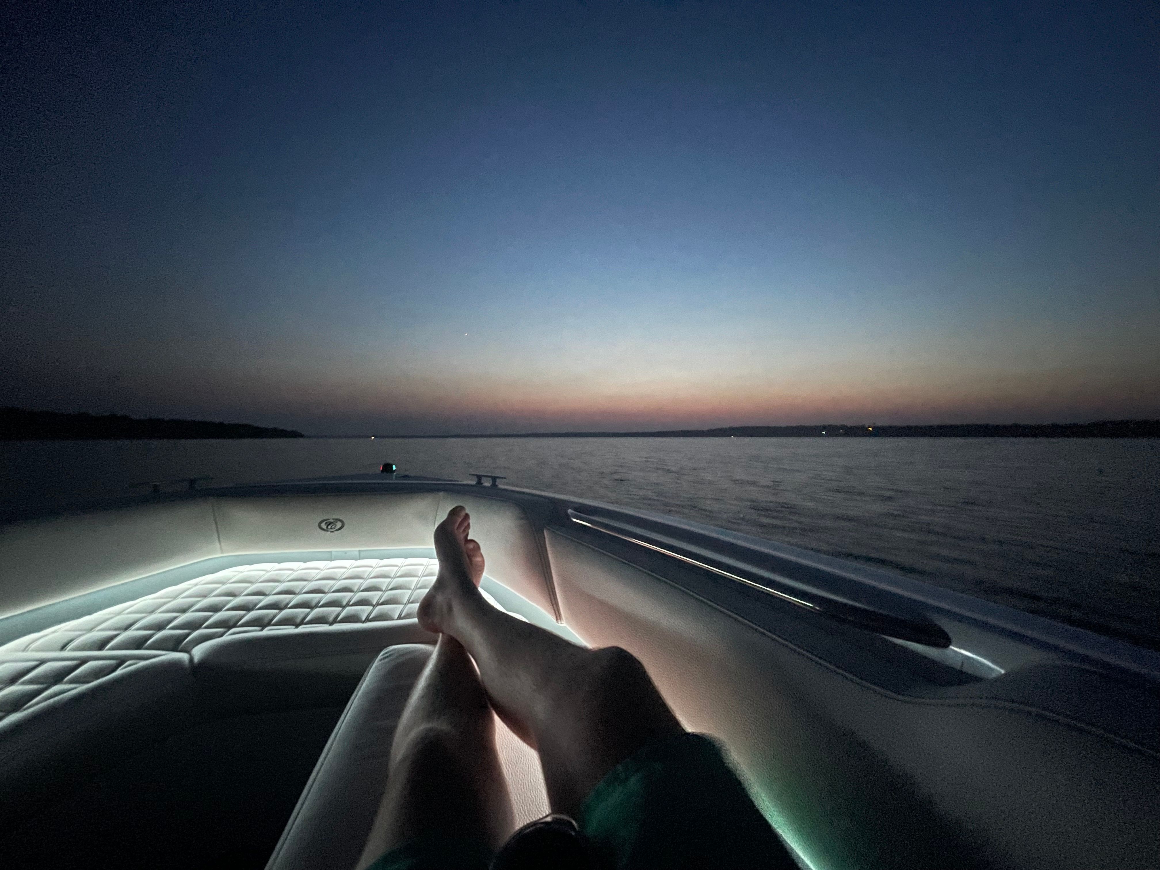 Person relaxing on a Cobalt R7 Surf boat at sunset over calm waters.
