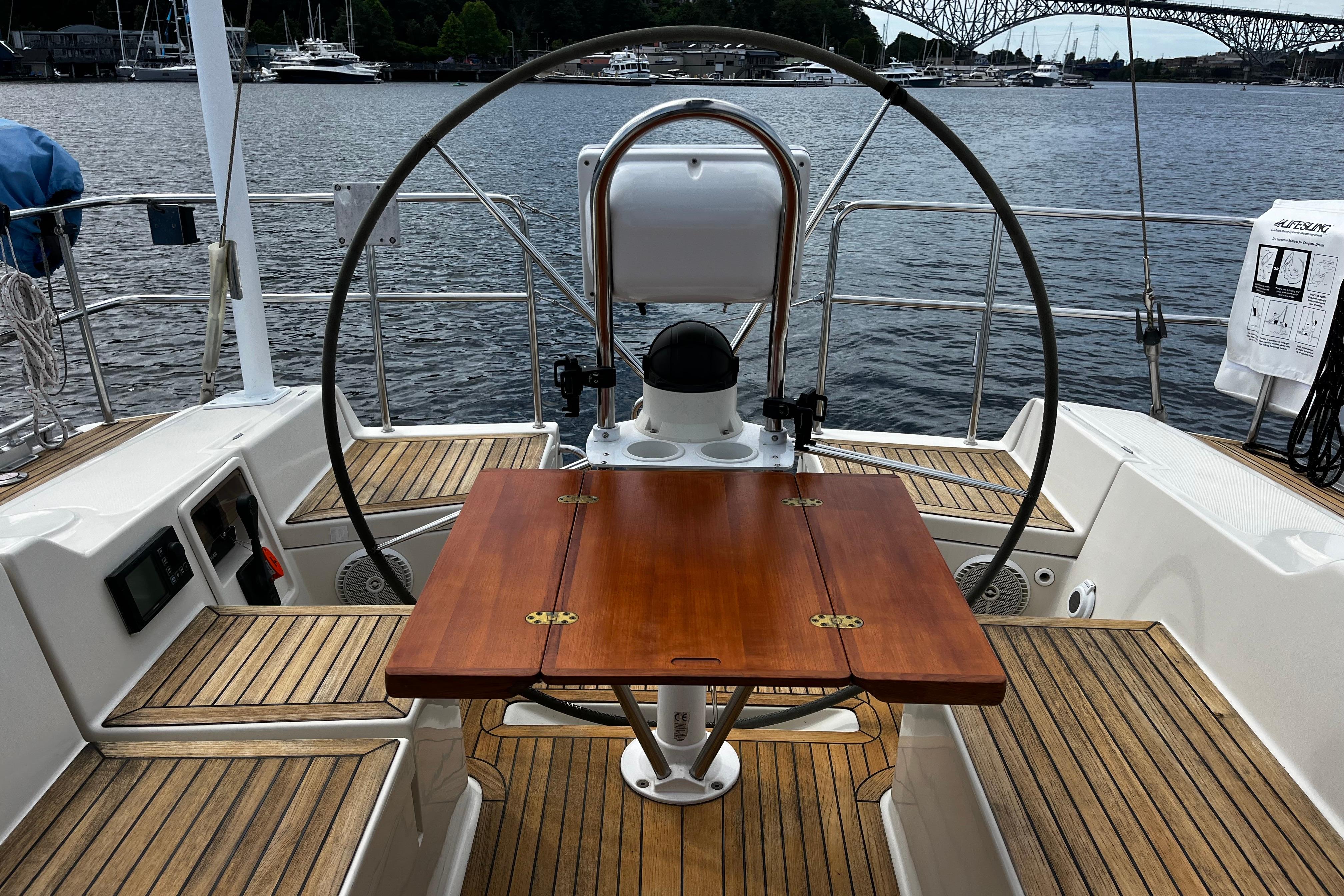 Cockpit of 2004 Hanse 411 sailboat with wooden table and steering wheel, docked by the water.