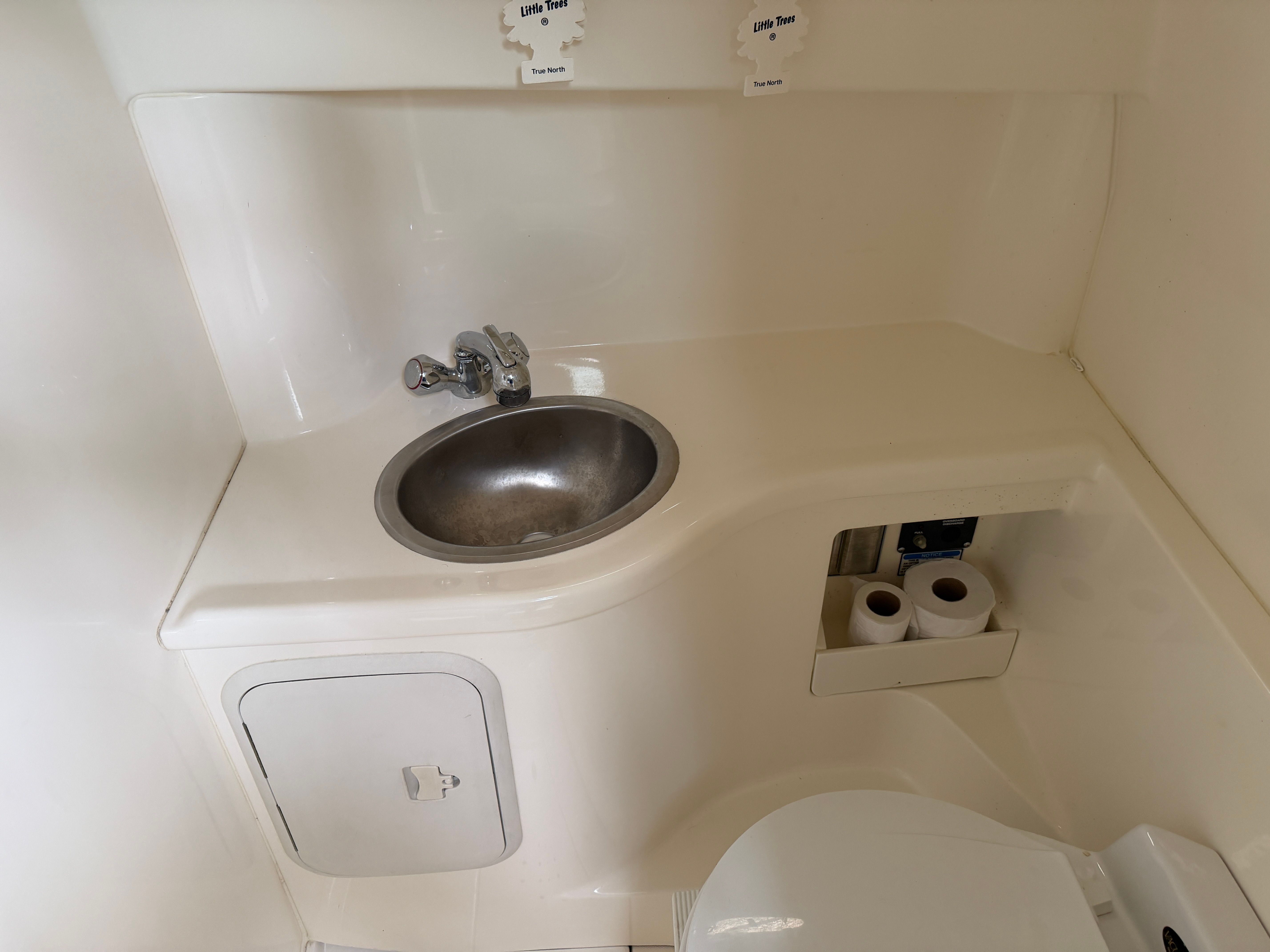 The image shows a clean, white bathroom on a boat with a sink and toilet.