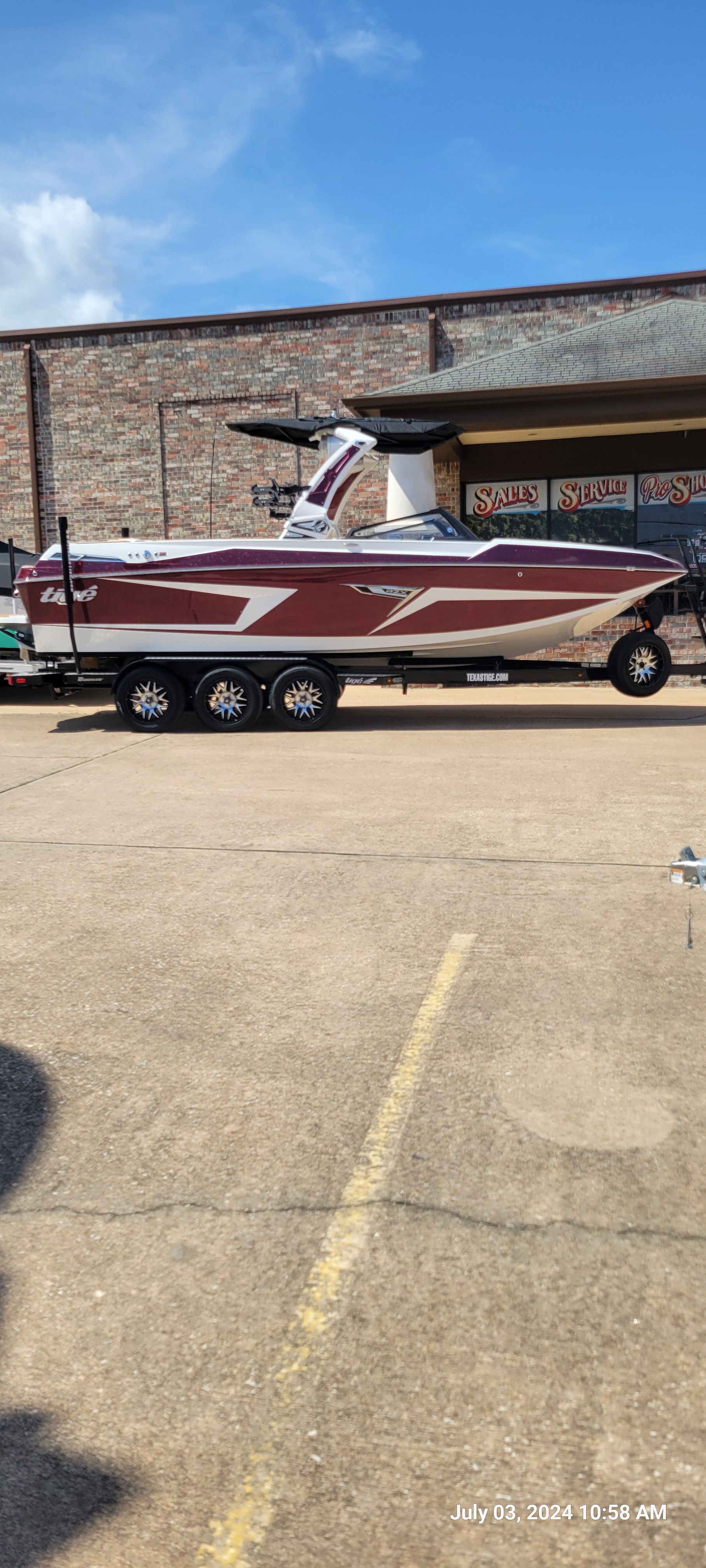 A 2023 Tigé 24RZX boat on a trailer, parked in a lot in front of a building.