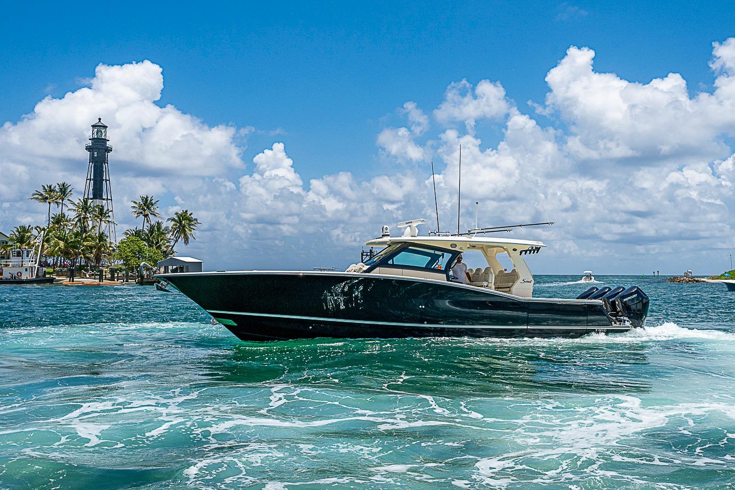 2025 Scout 425 LXF boat cruising near a lighthouse under a clear blue sky.