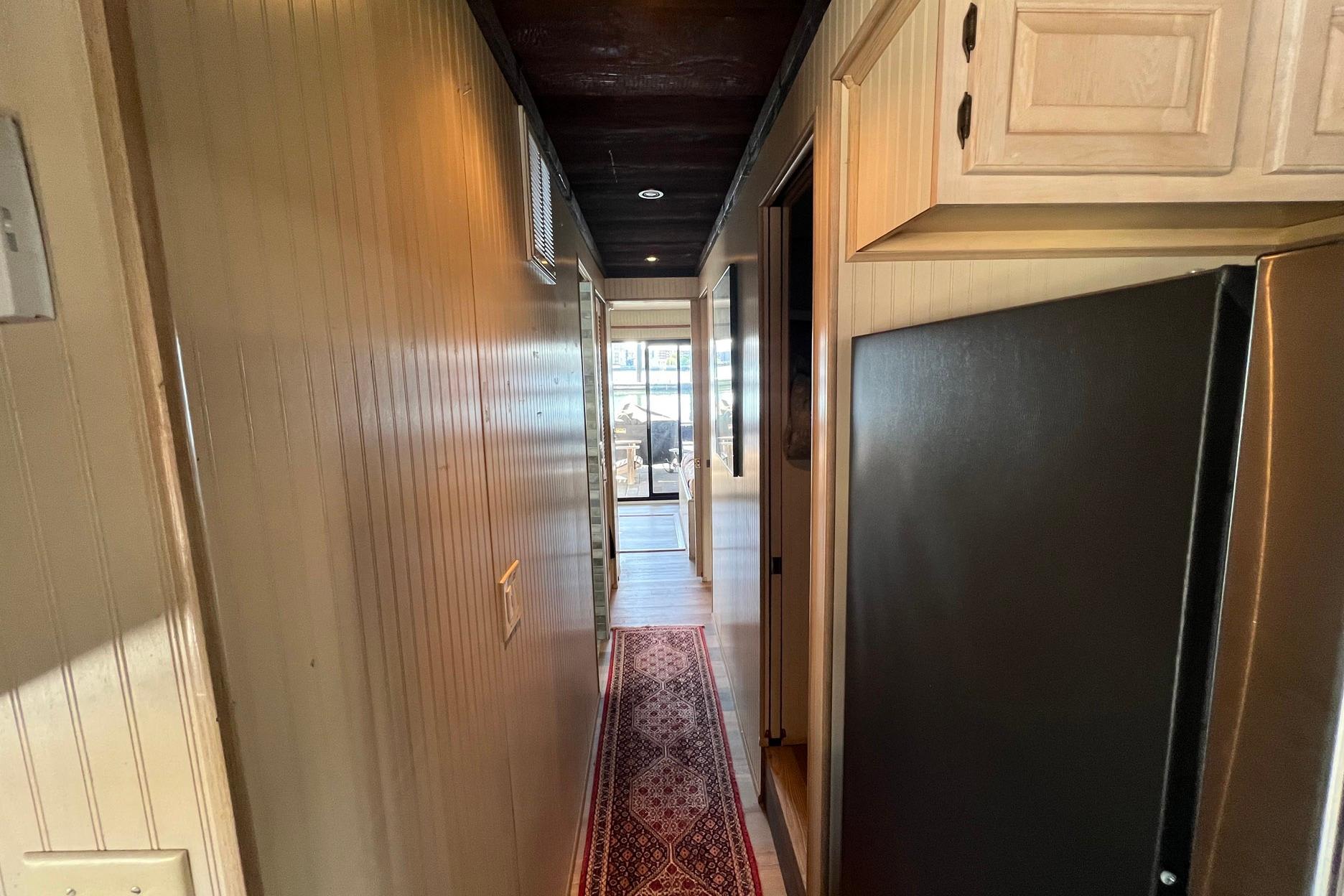 Narrow hallway inside a 1993 Sumerset houseboat with wooden cabinets and a patterned rug.