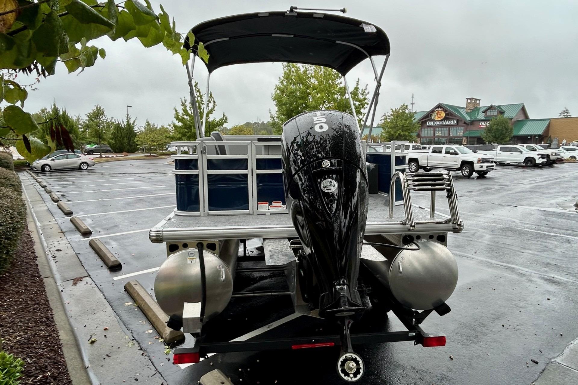 2026 Sun Tracker SportFish 22 DLX pontoon boat with outboard motor in parking lot.
