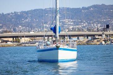 1989 Wauquiez Centurion 47 sailboat on calm water with cityscape background.