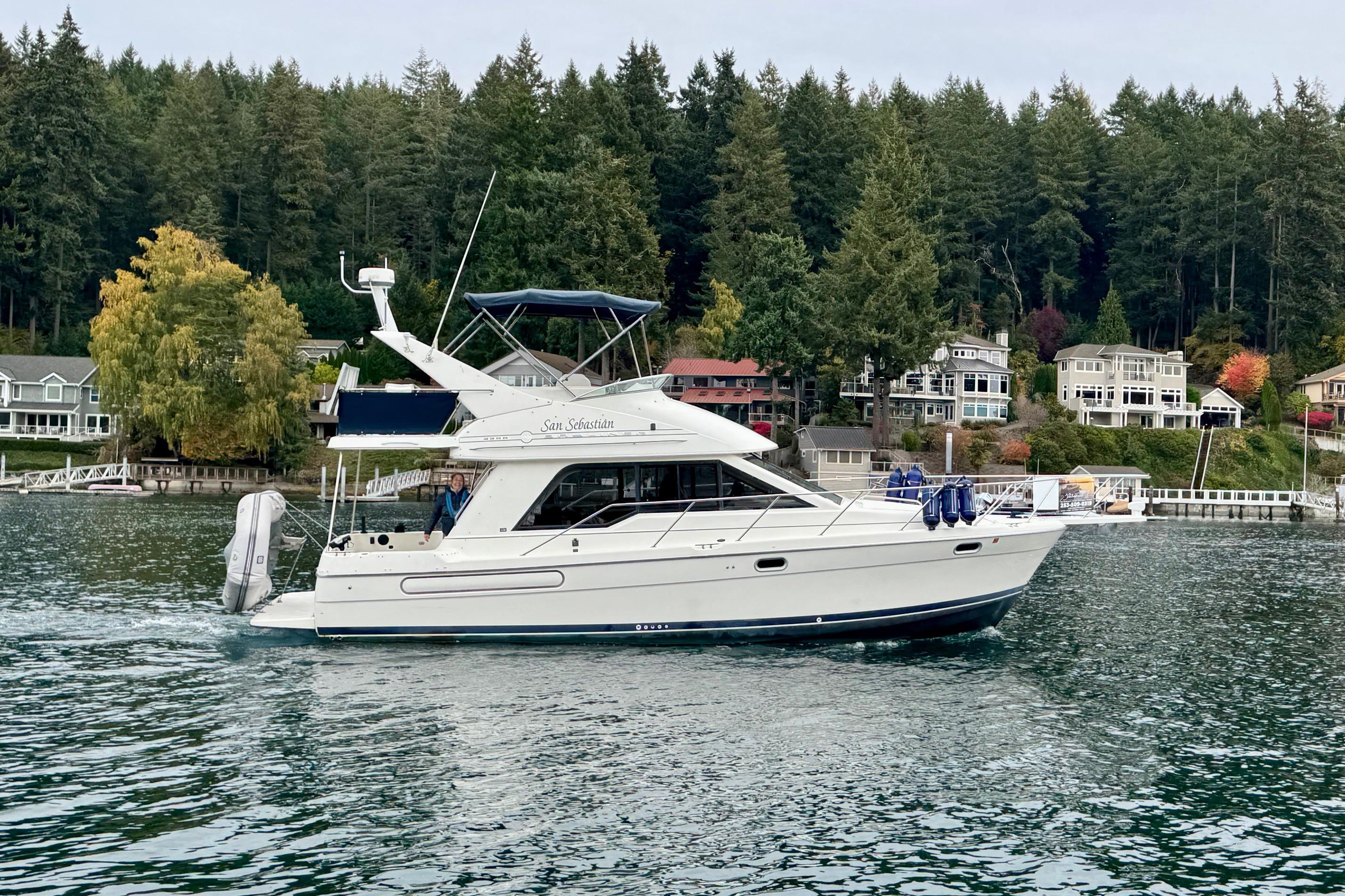 1998 Bayliner 3388 Command Bridge Motoryacht cruising near waterfront homes and lush forest.