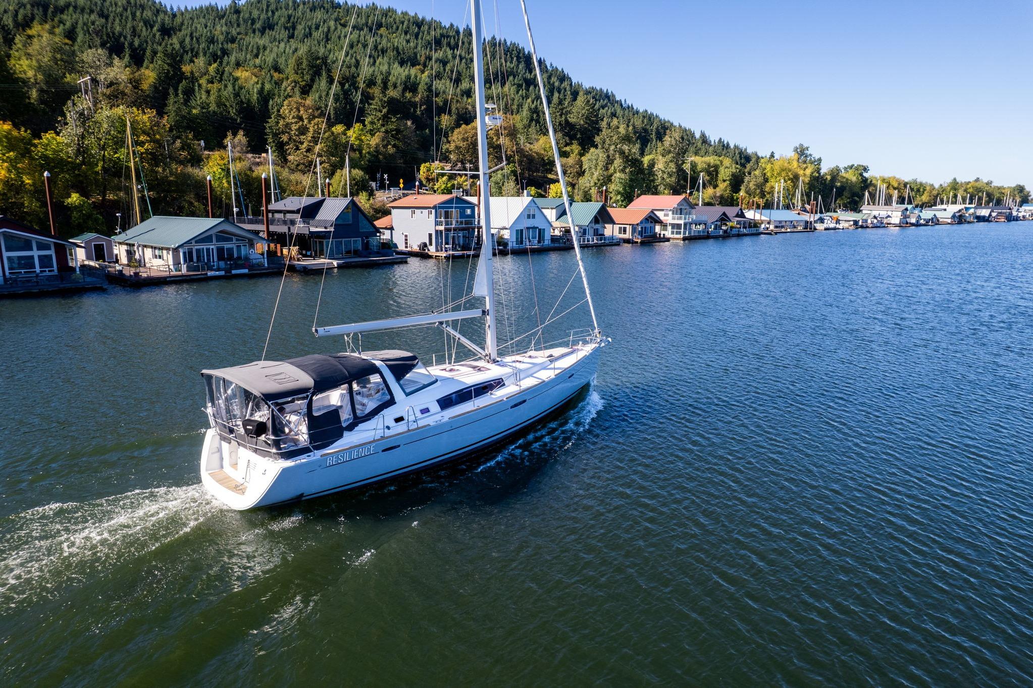 Beneteau Oceanis 50 sailboat cruising near colorful waterfront homes, surrounded by lush greenery.
