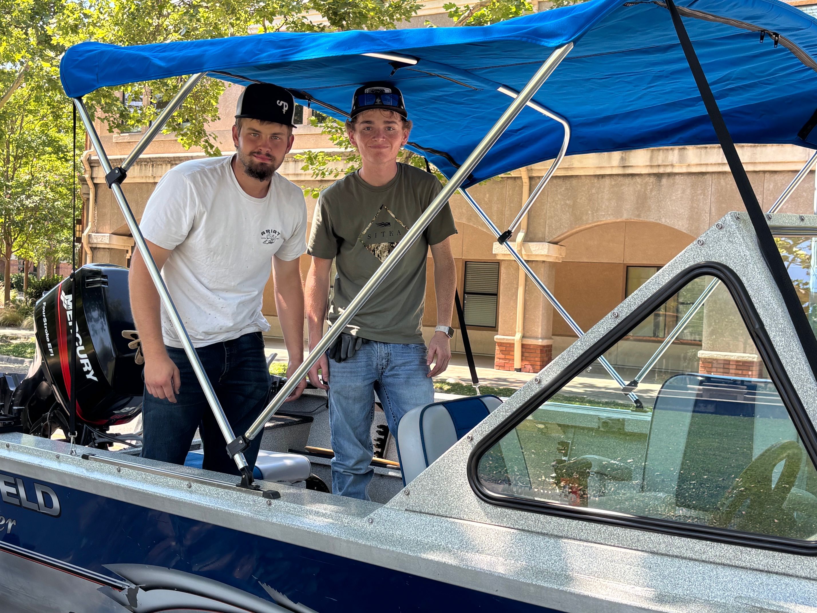 Two men stand on a blue boat with a blue sunshade.