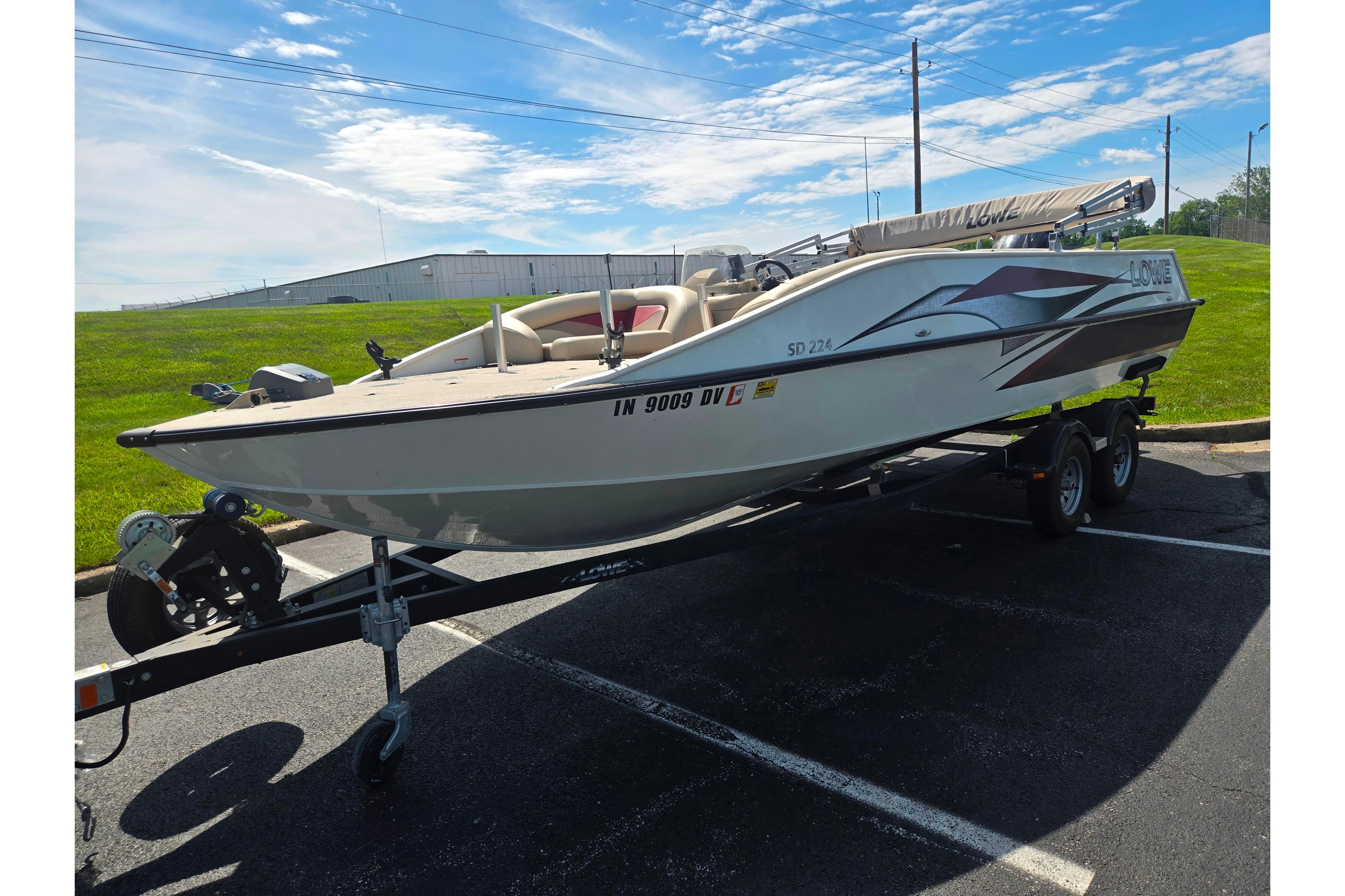 2015 Lowe Sport Deck 224 boat on trailer in parking lot under blue sky.