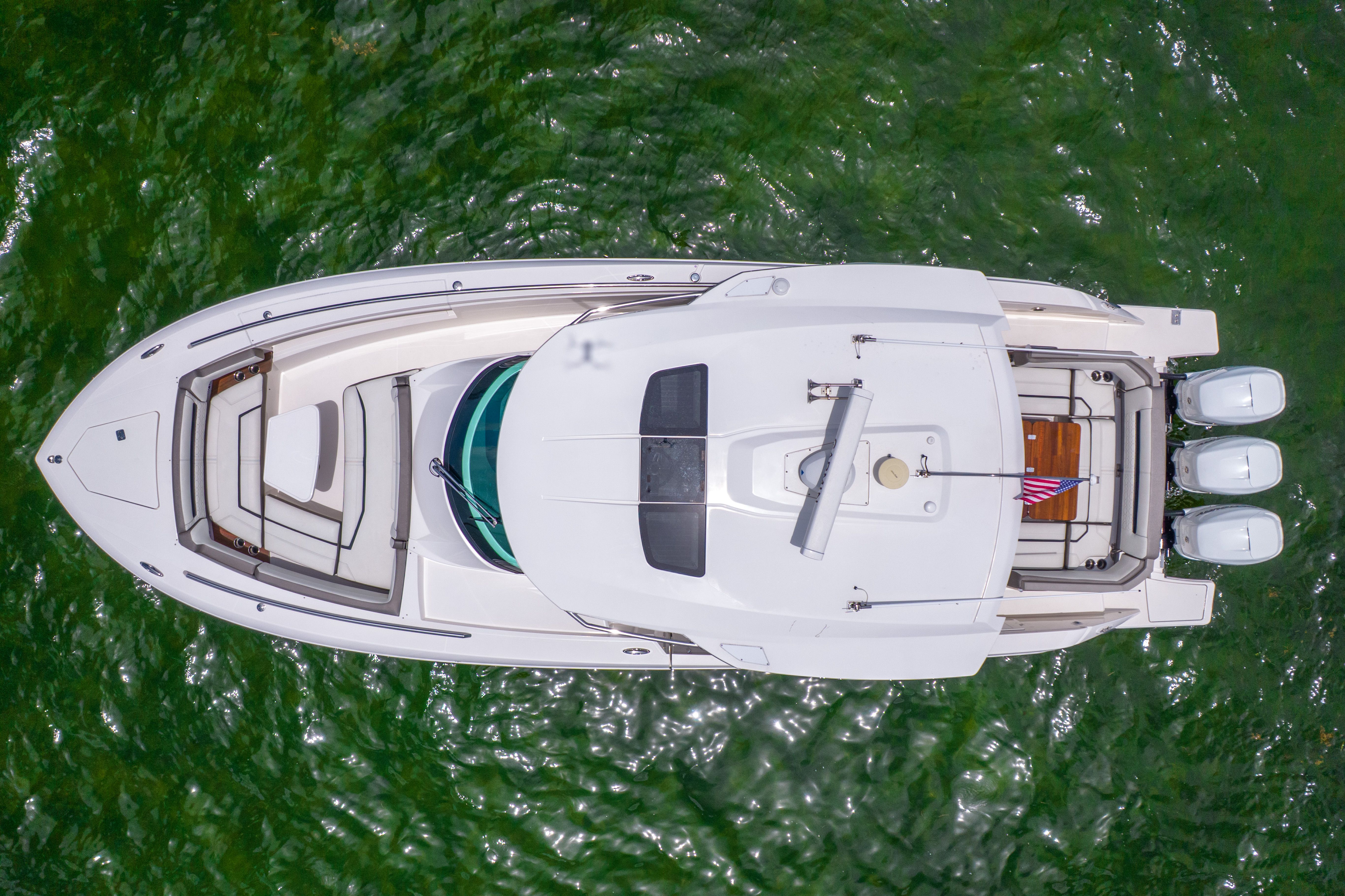 Aerial view of a luxurious white yacht on green water, featuring a spacious deck and three outboard engines.