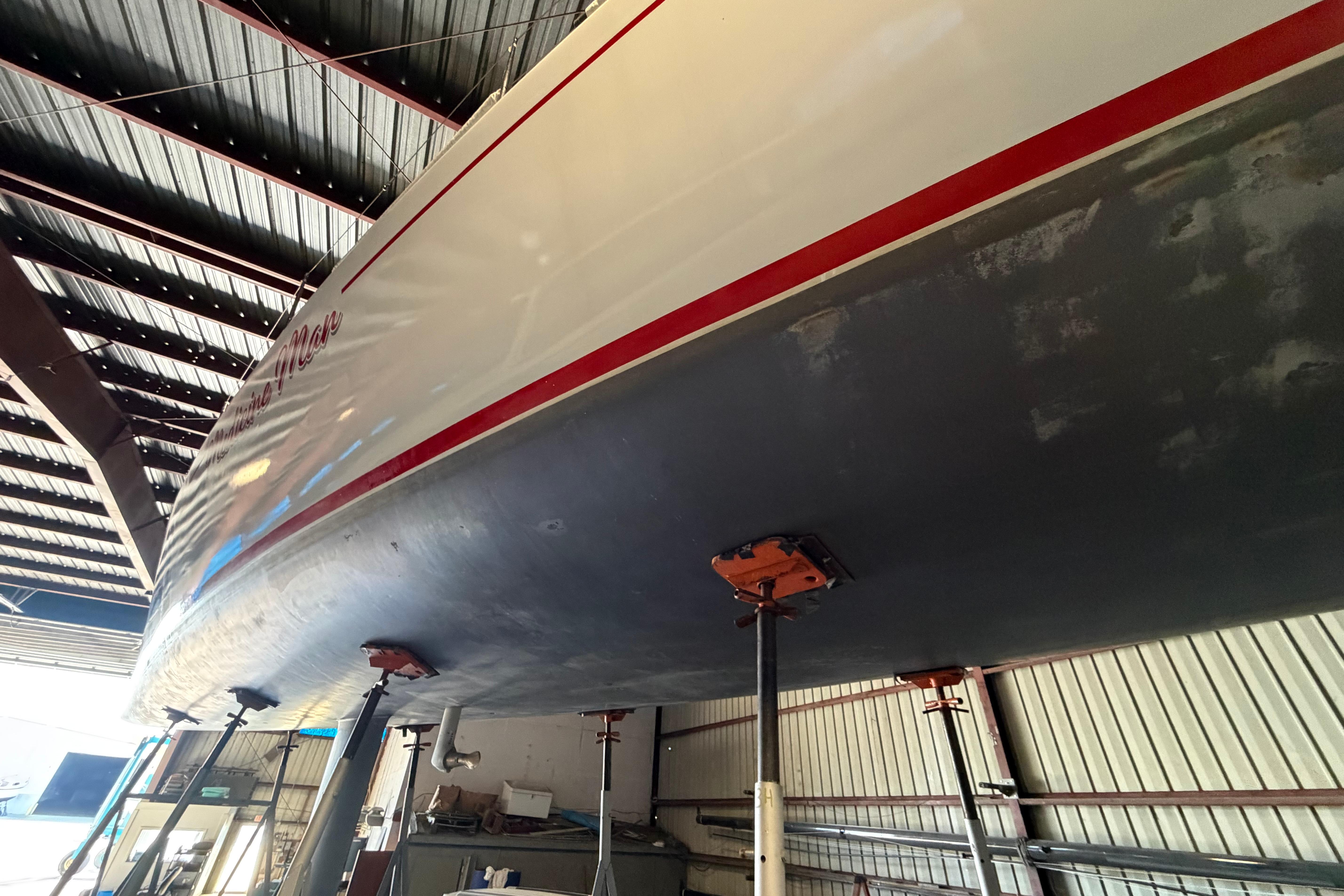 Andrews 63 yacht in dry dock, underside view, supported by stands in a metal-roofed shed.