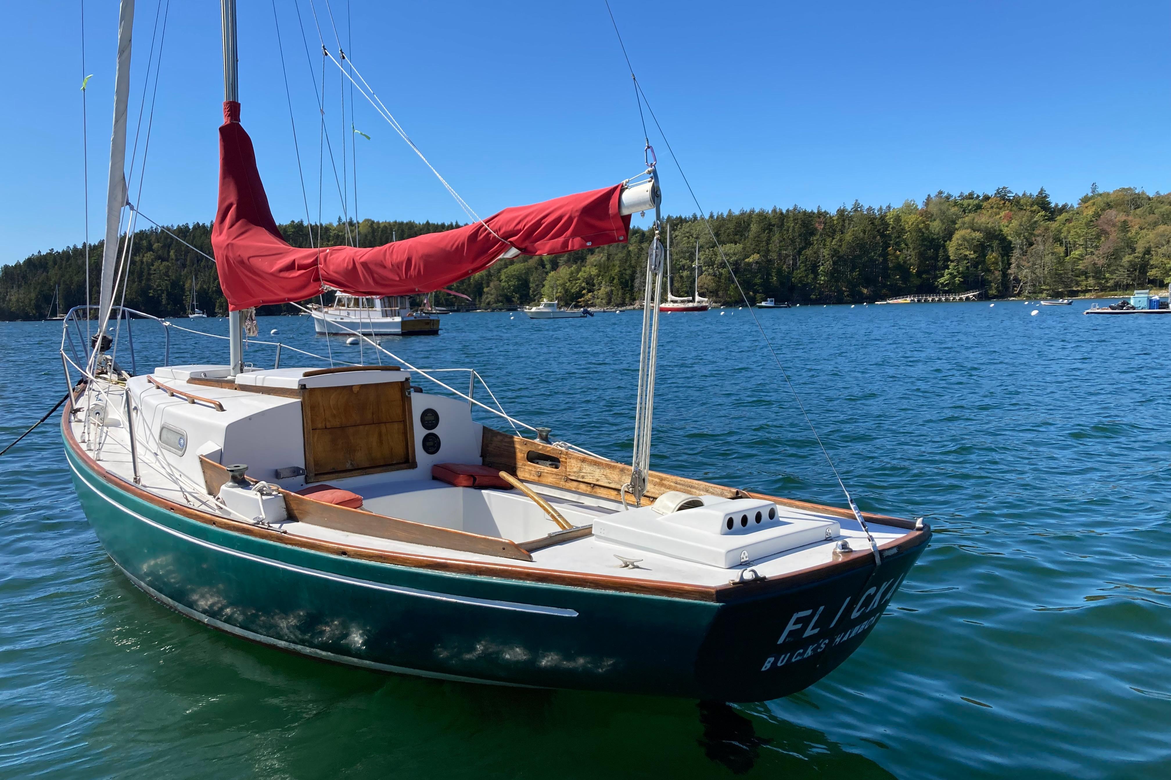 Vintage 1969 Allied Greenwich 24 sailboat with red sail, docked on a serene lake.