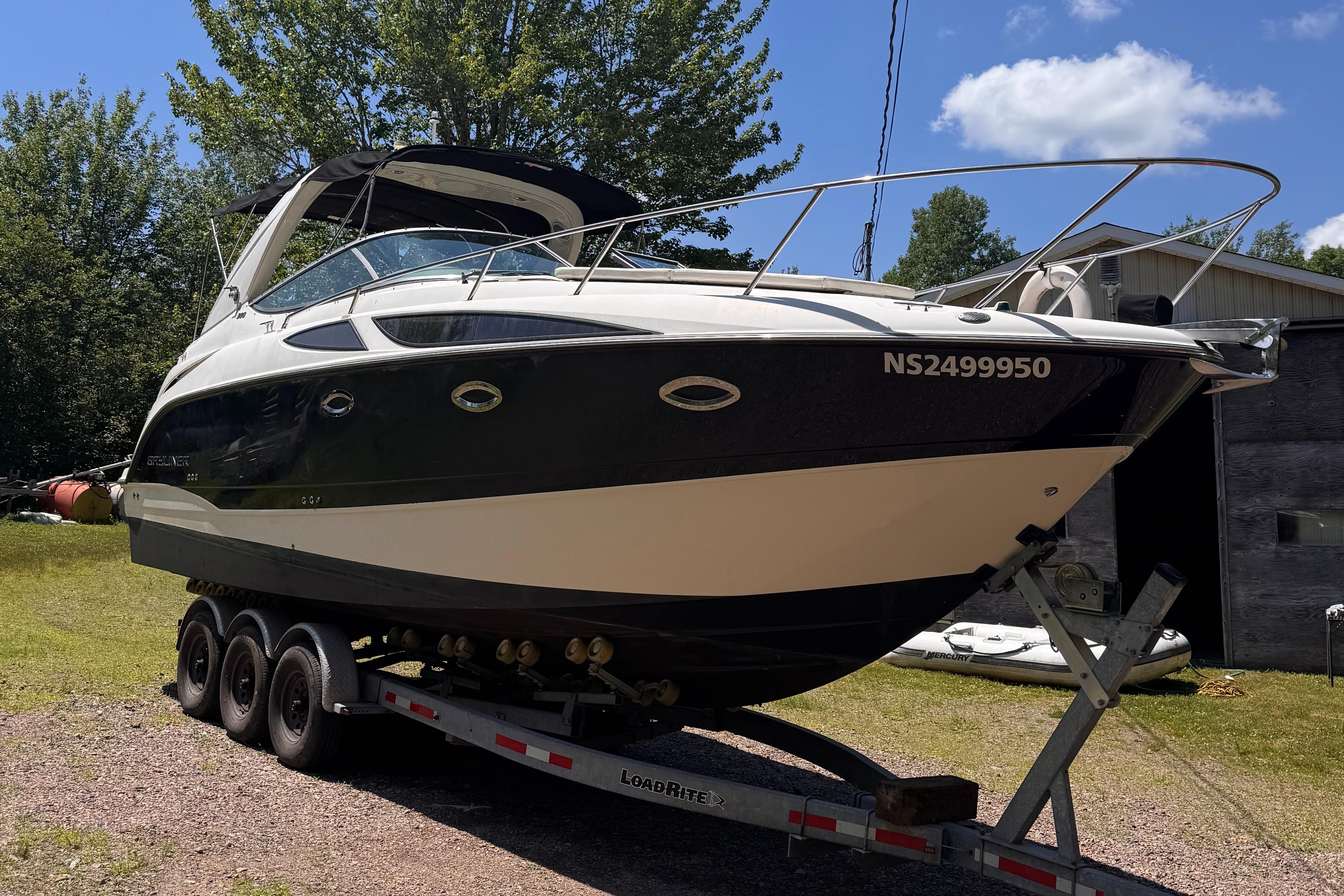 2009 Bayliner 300 boat on trailer, parked outdoors with trees and blue sky background.