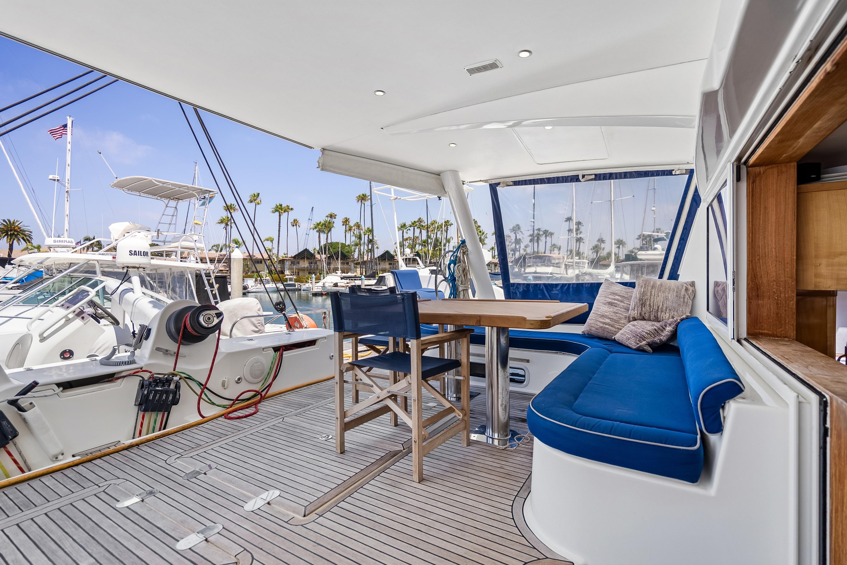 Luxurious 2009 Catana 65 yacht deck with blue seating, wooden table, and marina view.