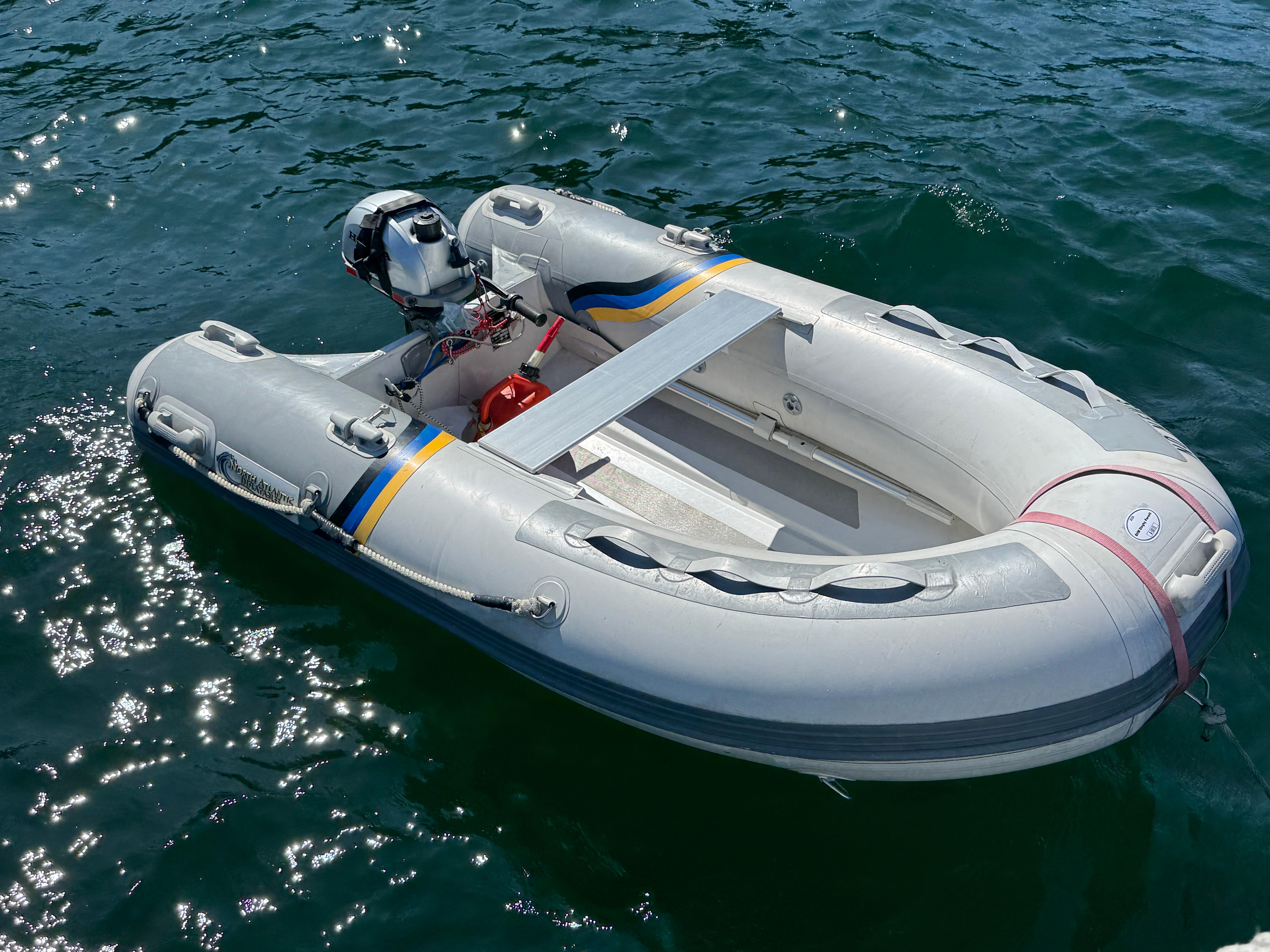 Inflatable dinghy with outboard motor floating on water, sunny day.