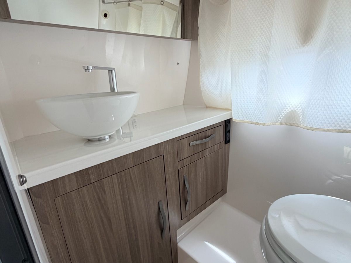 Interior view of a boat with a sink and toilet, modern wood cabinets, and curtains.