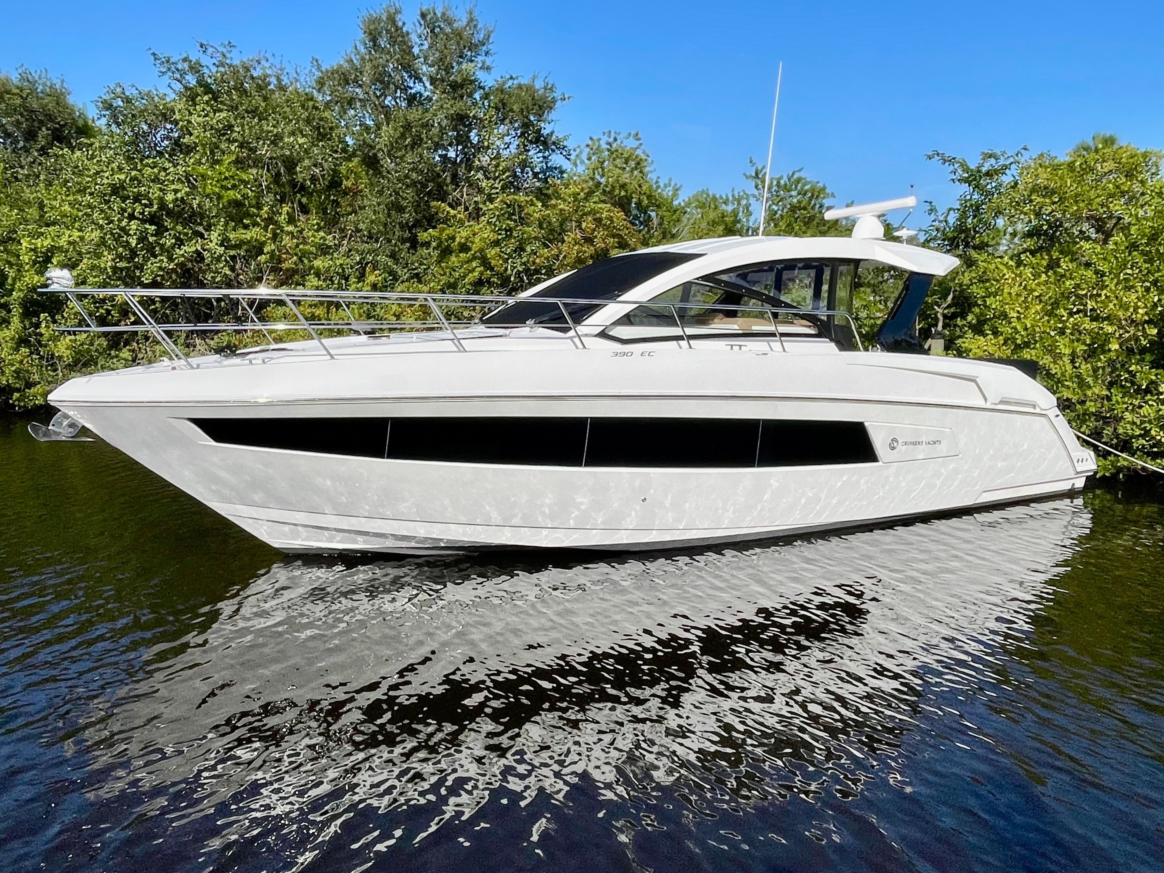 A luxurious white yacht floating on calm water with a green shoreline backdrop.
