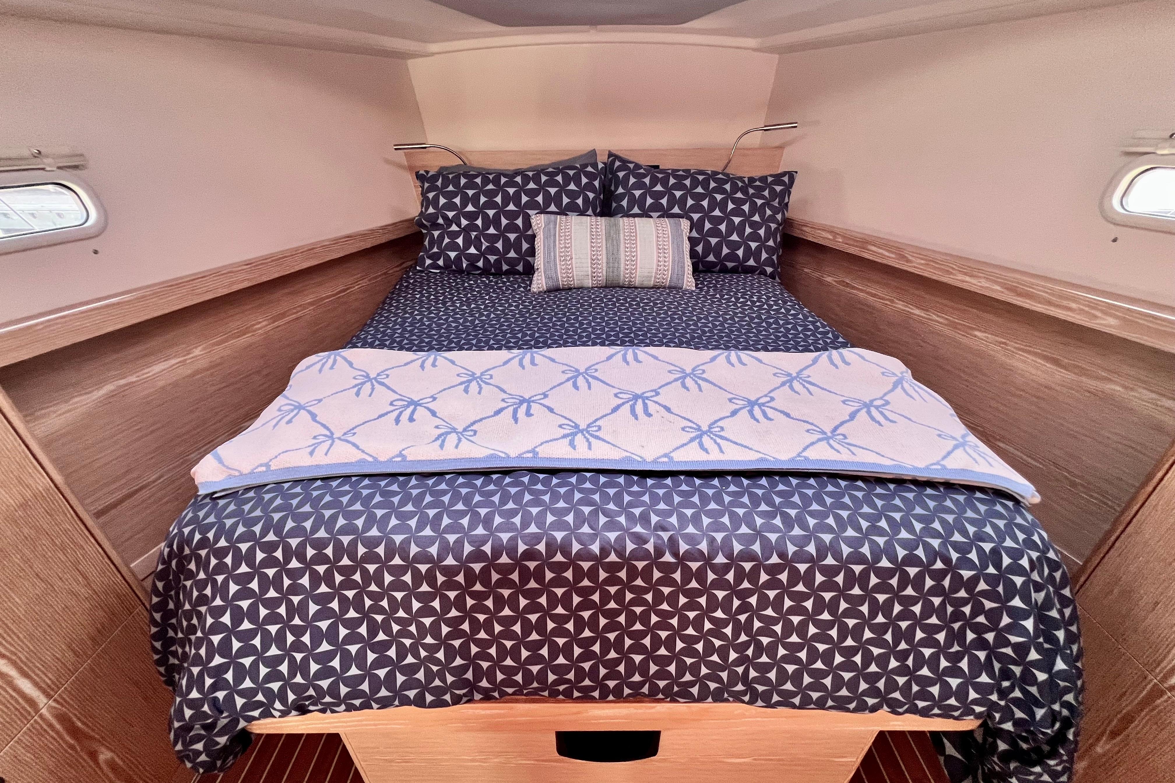 Cozy cabin interior of 2016 Hanse 455 yacht with patterned bedding and wooden accents.