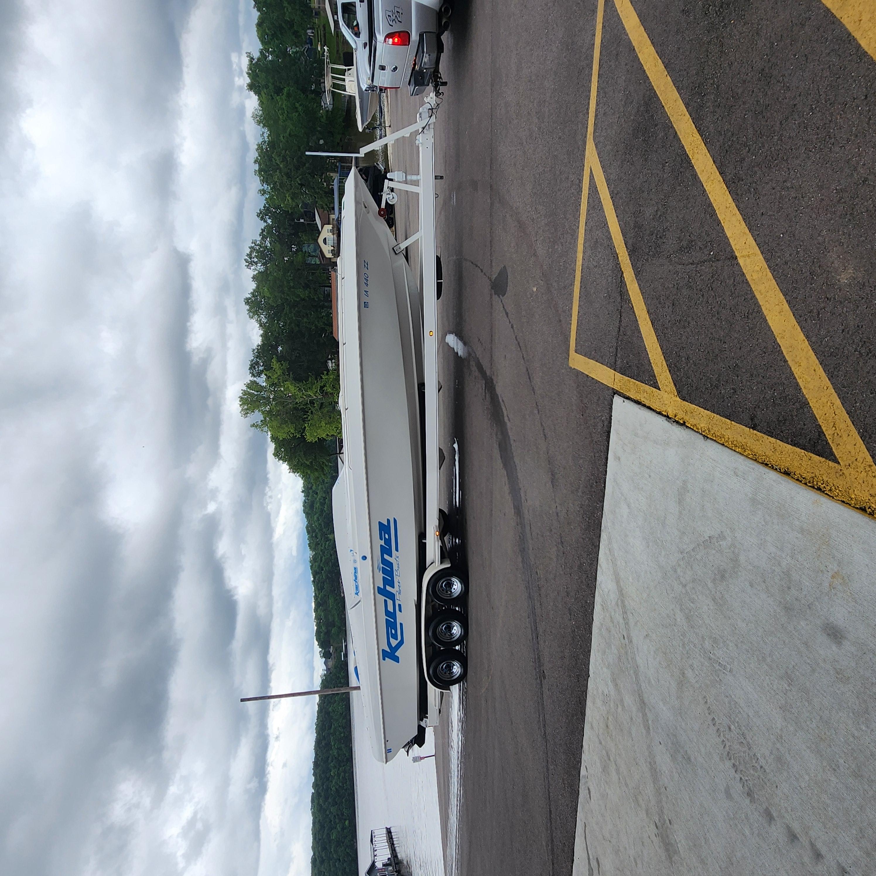 2005 Kachina Bolero boat on trailer, parked near a lake under cloudy skies.
