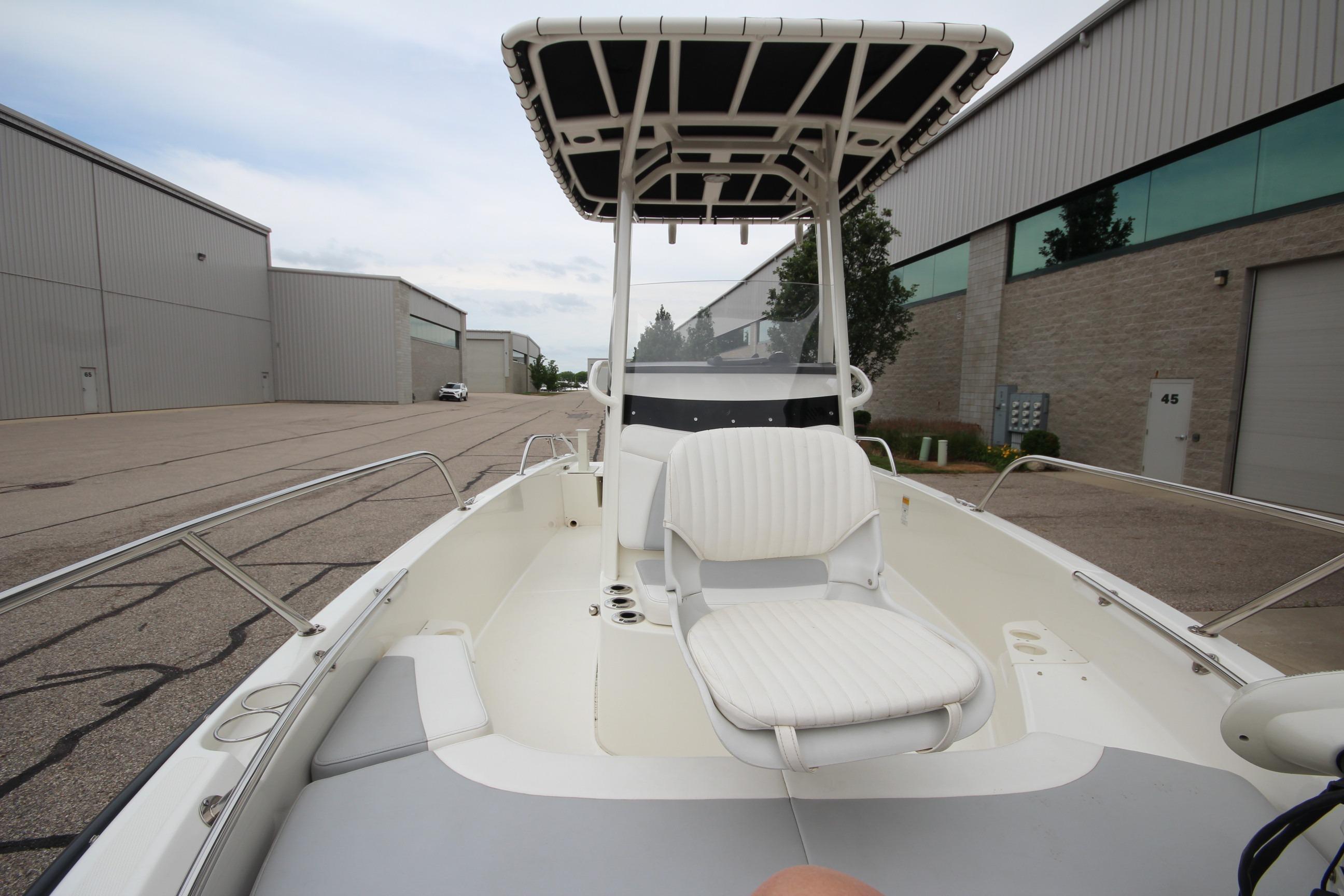 2014 Boston Whaler 210 Dauntless boat with T-top, docked near industrial buildings.