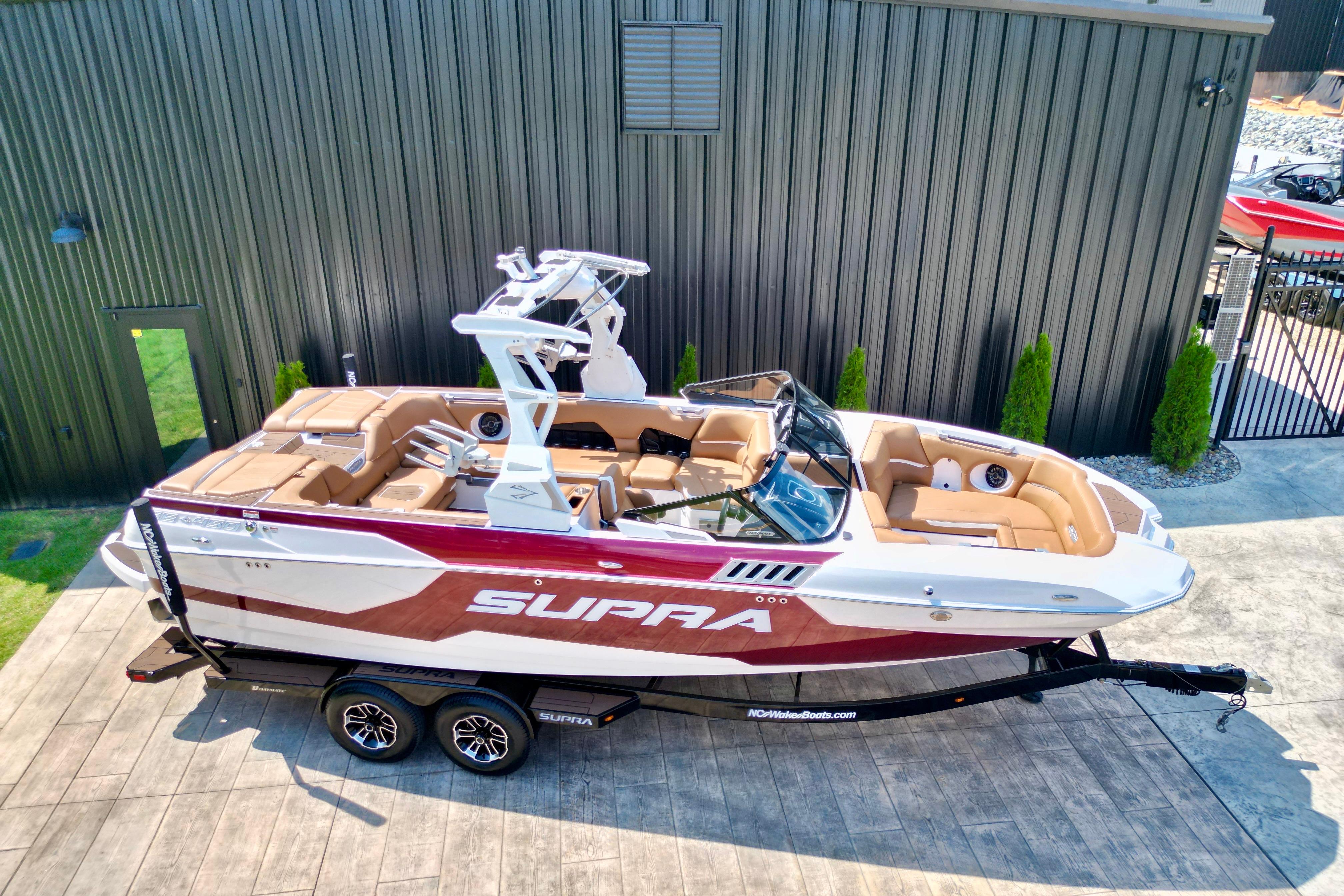 2021 Supra SE boat with red and white design, parked on a trailer near a building.