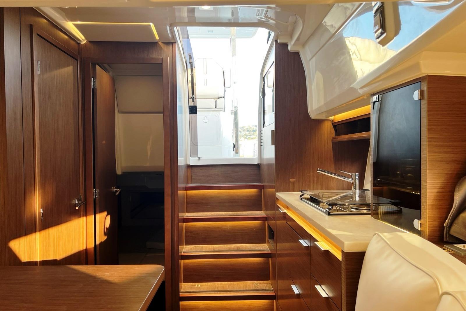Interior of 2021 Jeanneau Cap Camarat 10.5 WA Serie 2, featuring modern wood finishes and compact kitchen.