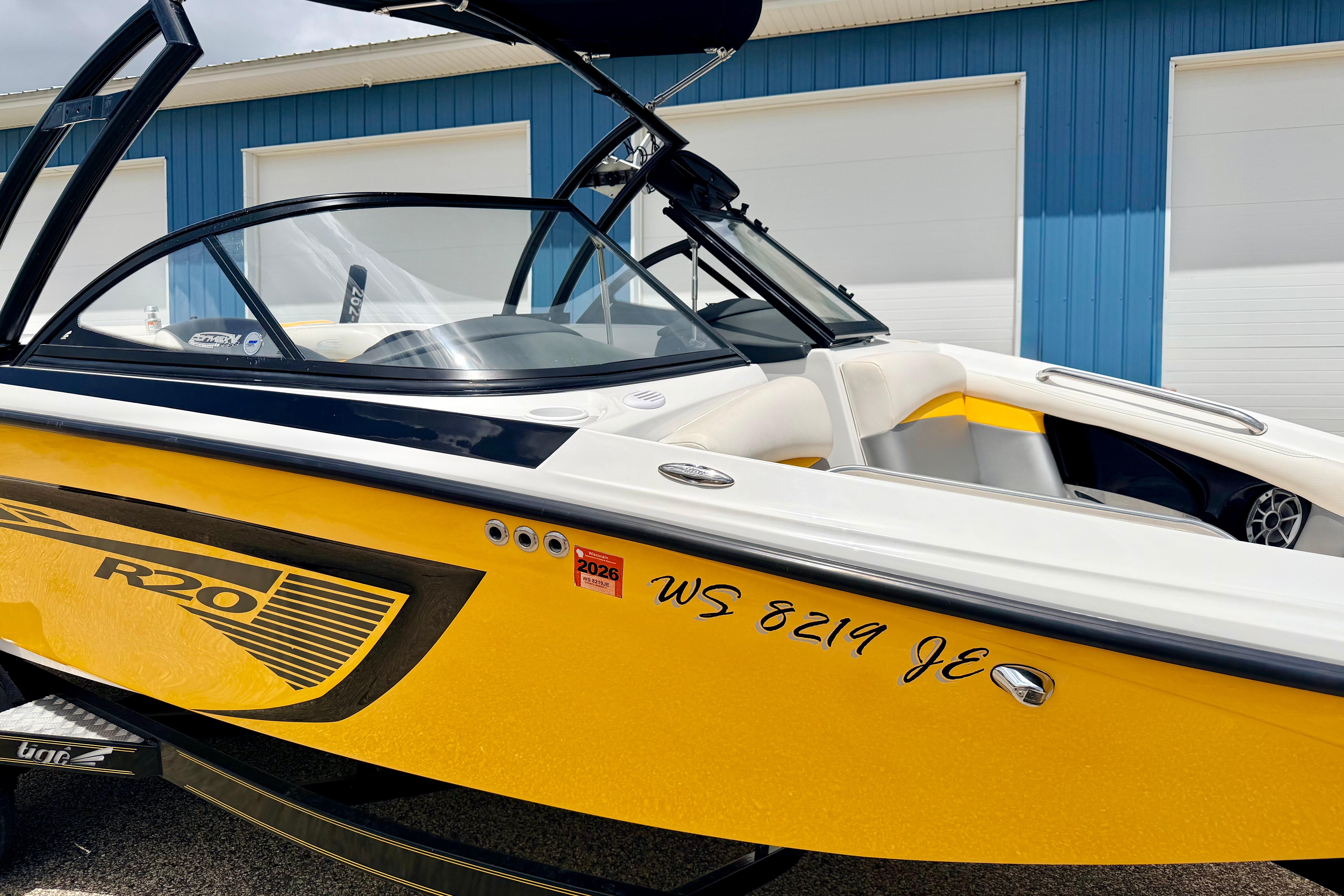2014 Tigé R20 boat with yellow and black design, parked near a blue building.