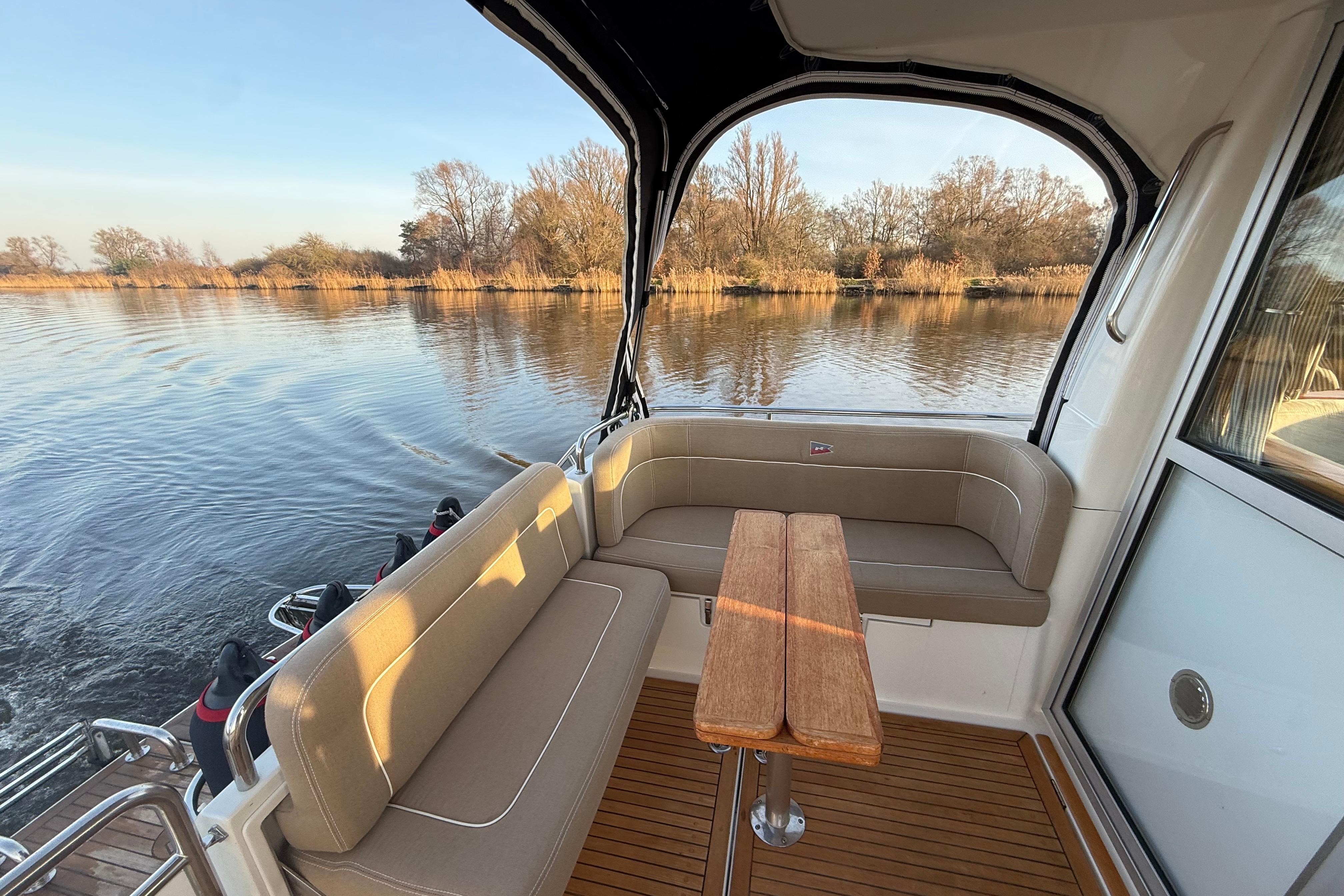 Nimbus 335 Coupe 2011 boat interior with seating and table, overlooking serene water and trees.