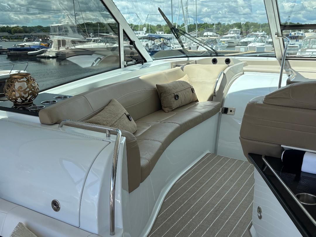 Interior view of a luxury yacht with beige leather seating and cushions, surrounded by other boats in a marina.