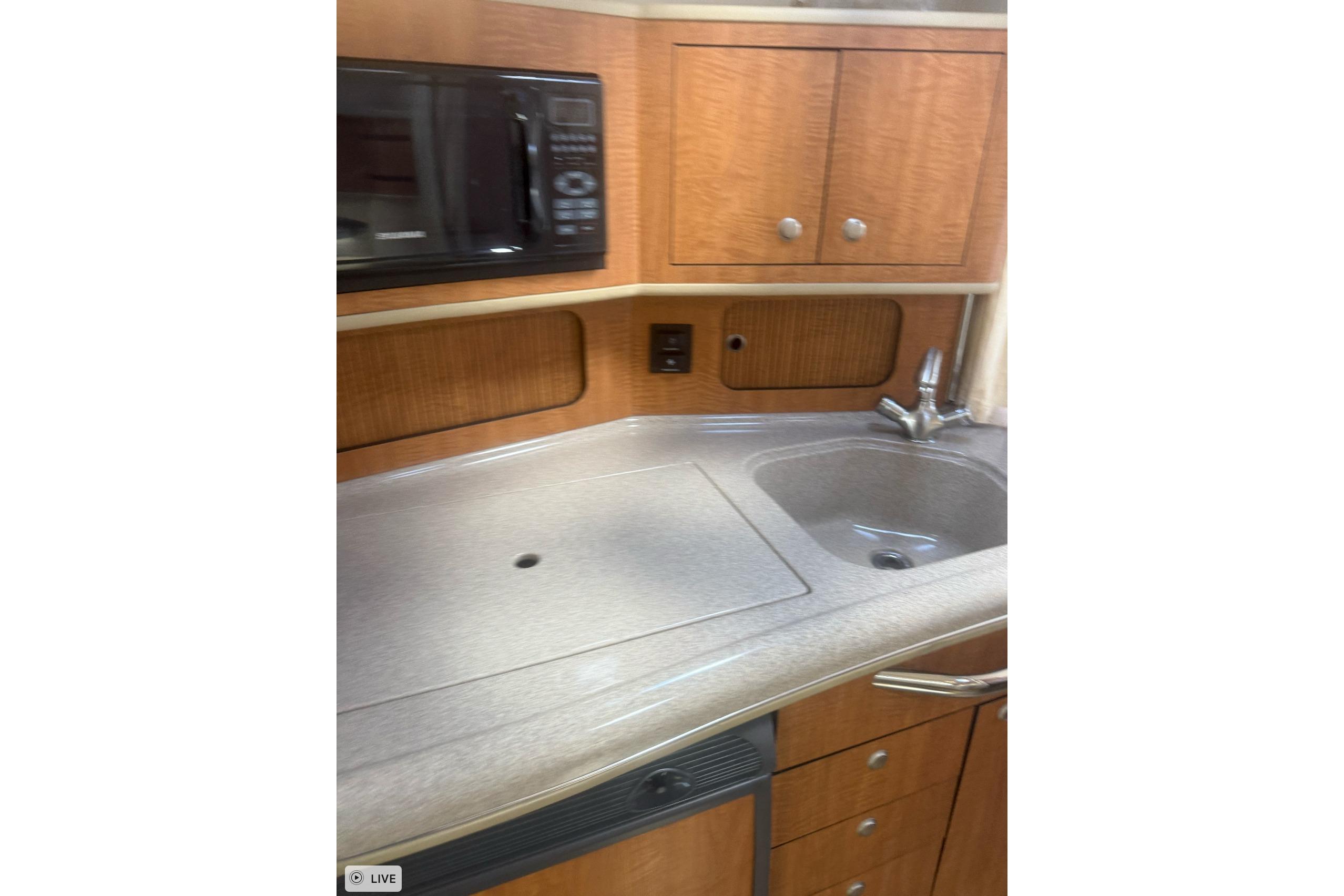 2006 Sea Ray 300 Sundancer galley with sink, microwave, and wooden cabinetry.