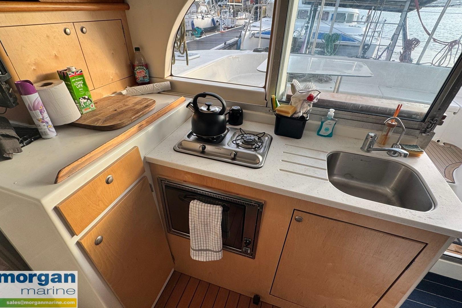 Compact kitchen in 2004 Lagoon 380 Catamaran, featuring stove, sink, and wooden cabinetry.
