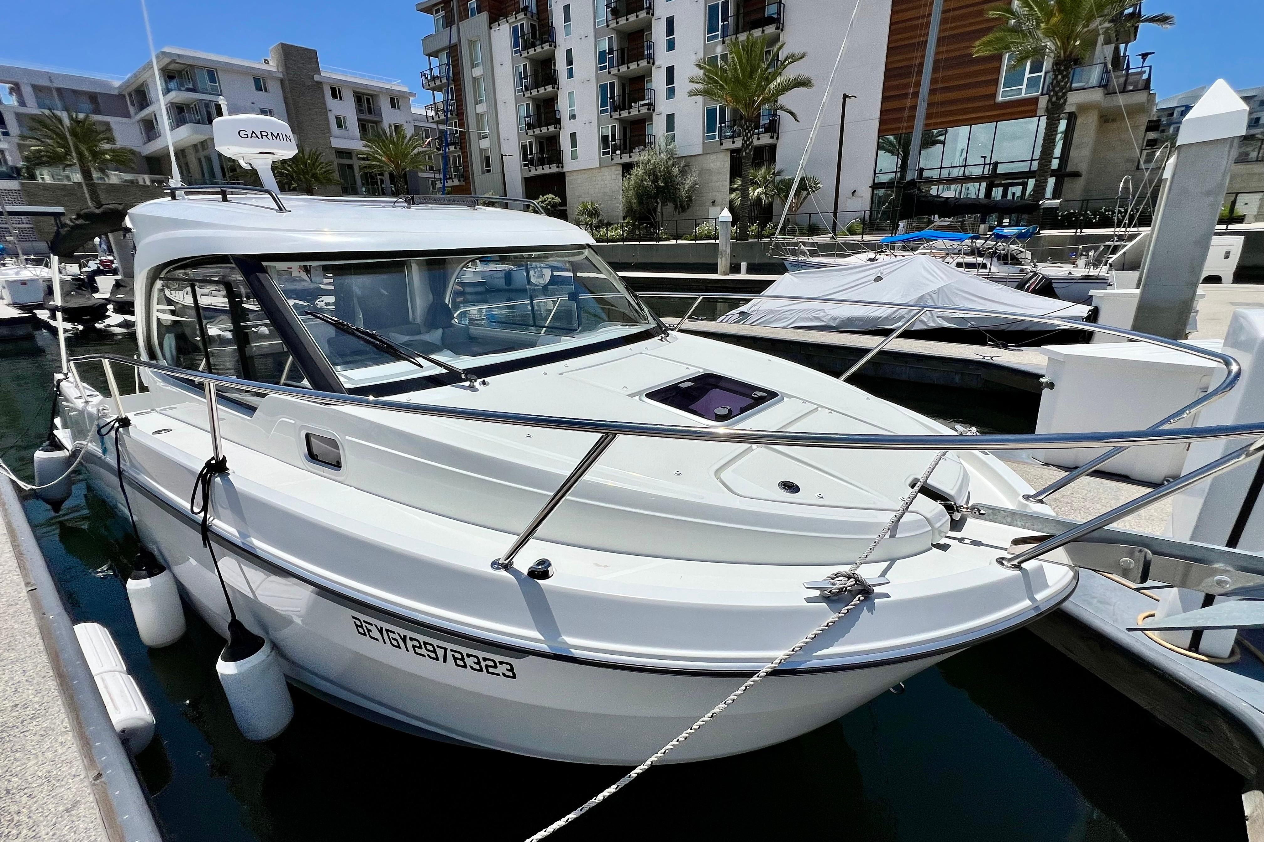 2023 Beneteau Antares 8 docked at a marina, surrounded by modern buildings.