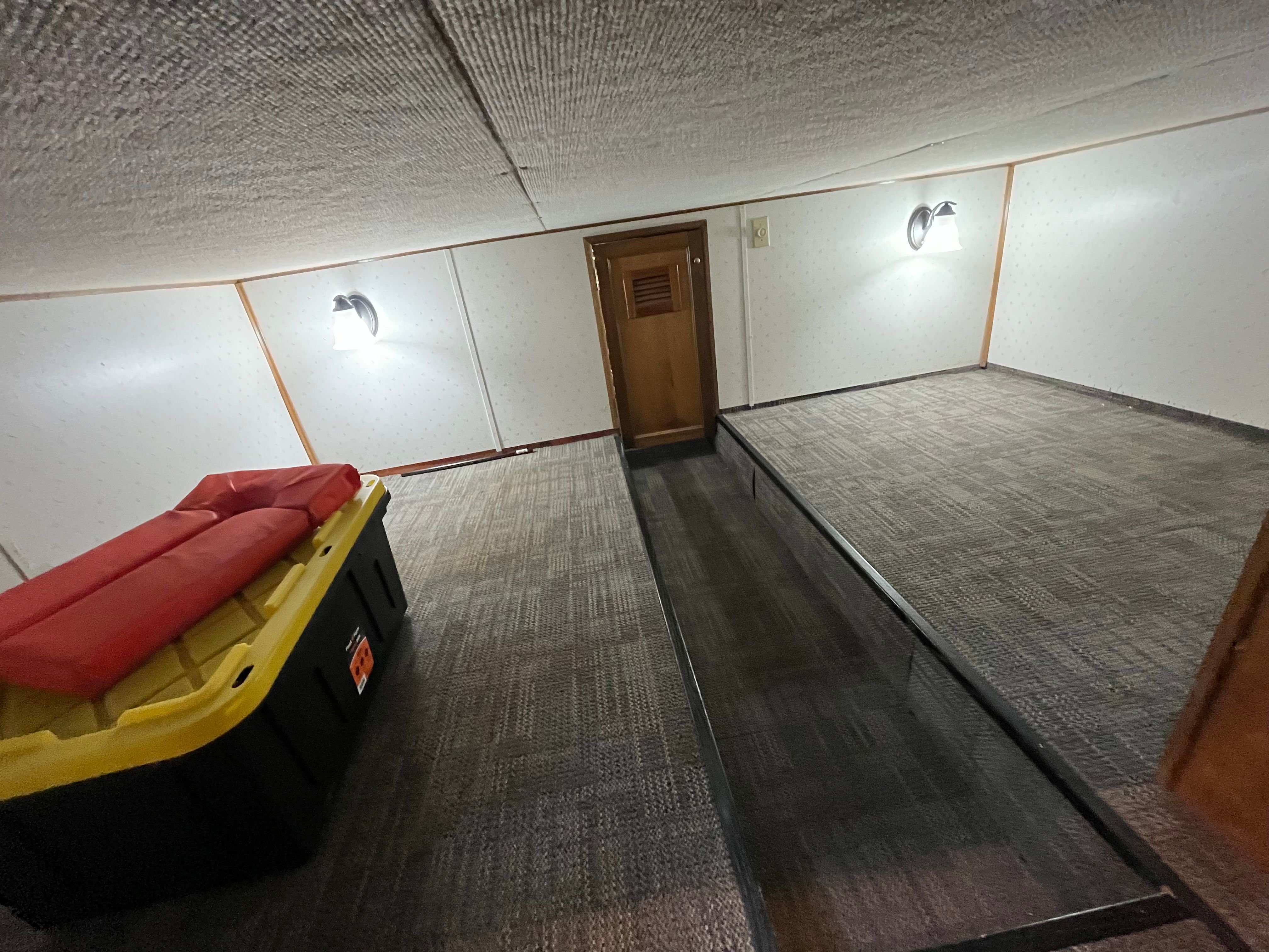 Interior of a boat with carpeted floor, a yellow storage bin, and red cushions.