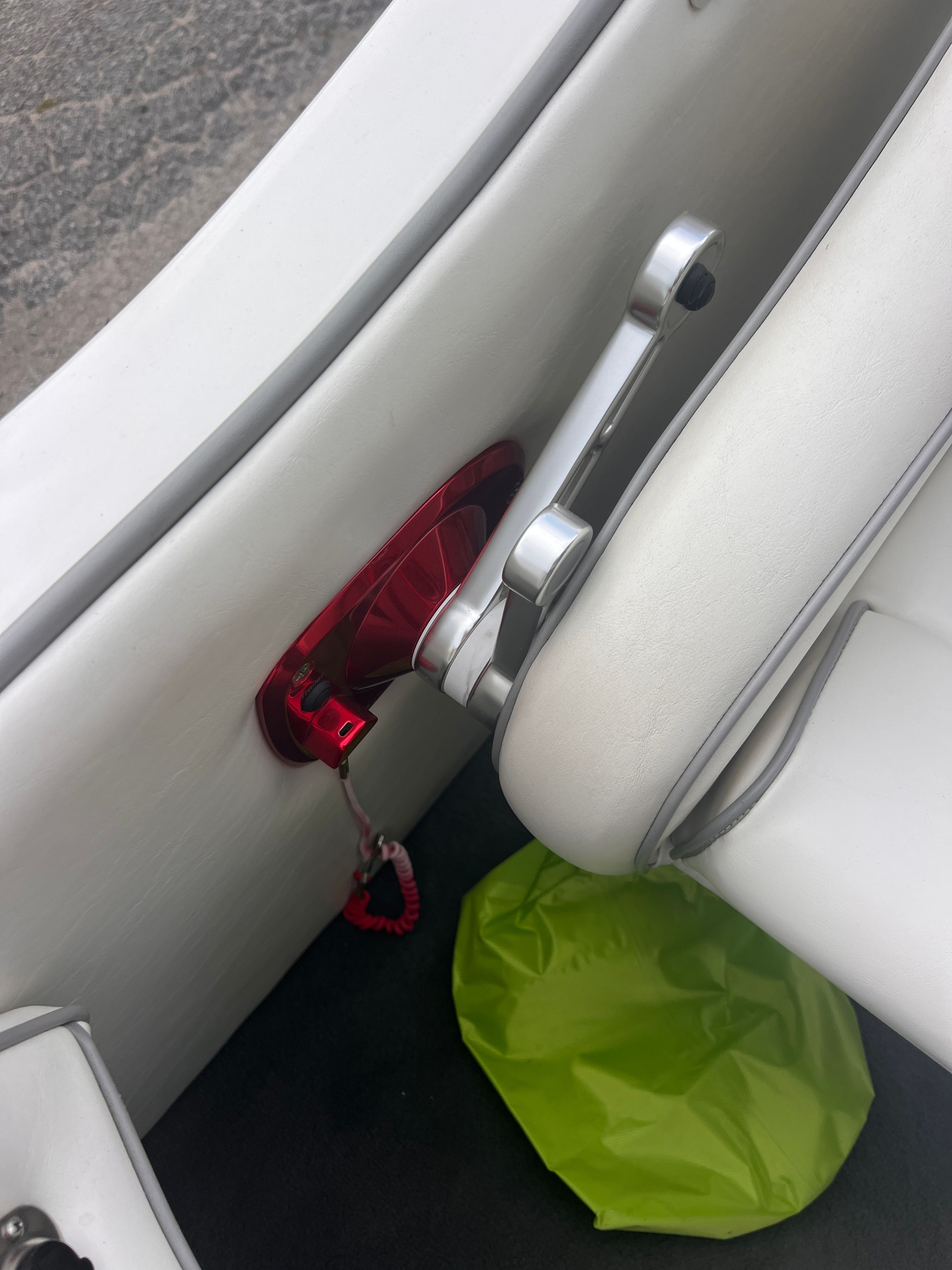 Close-up of a white boat seat with a red handle and a green item on the floor.