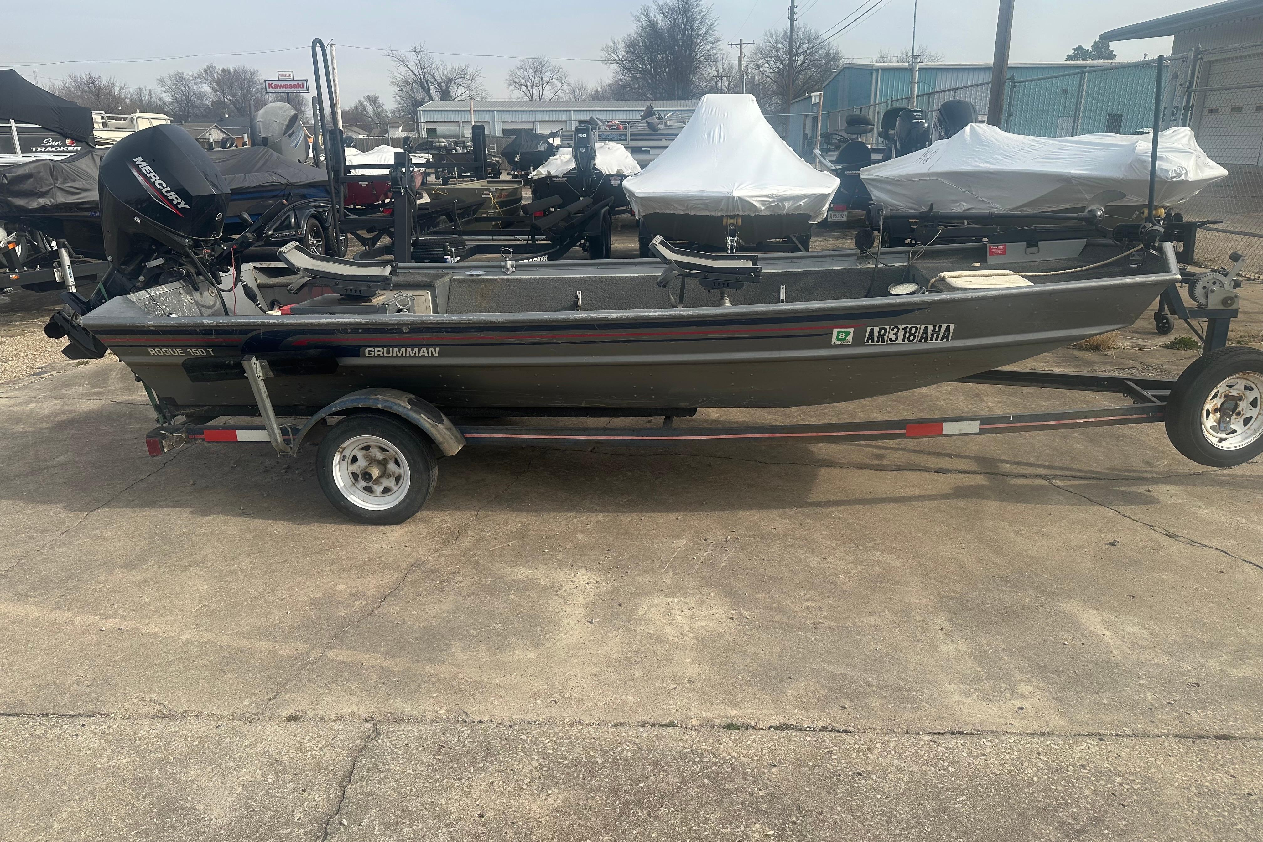 1991 Grumman Rogue 150 T boat on trailer, parked outdoors with other boats.