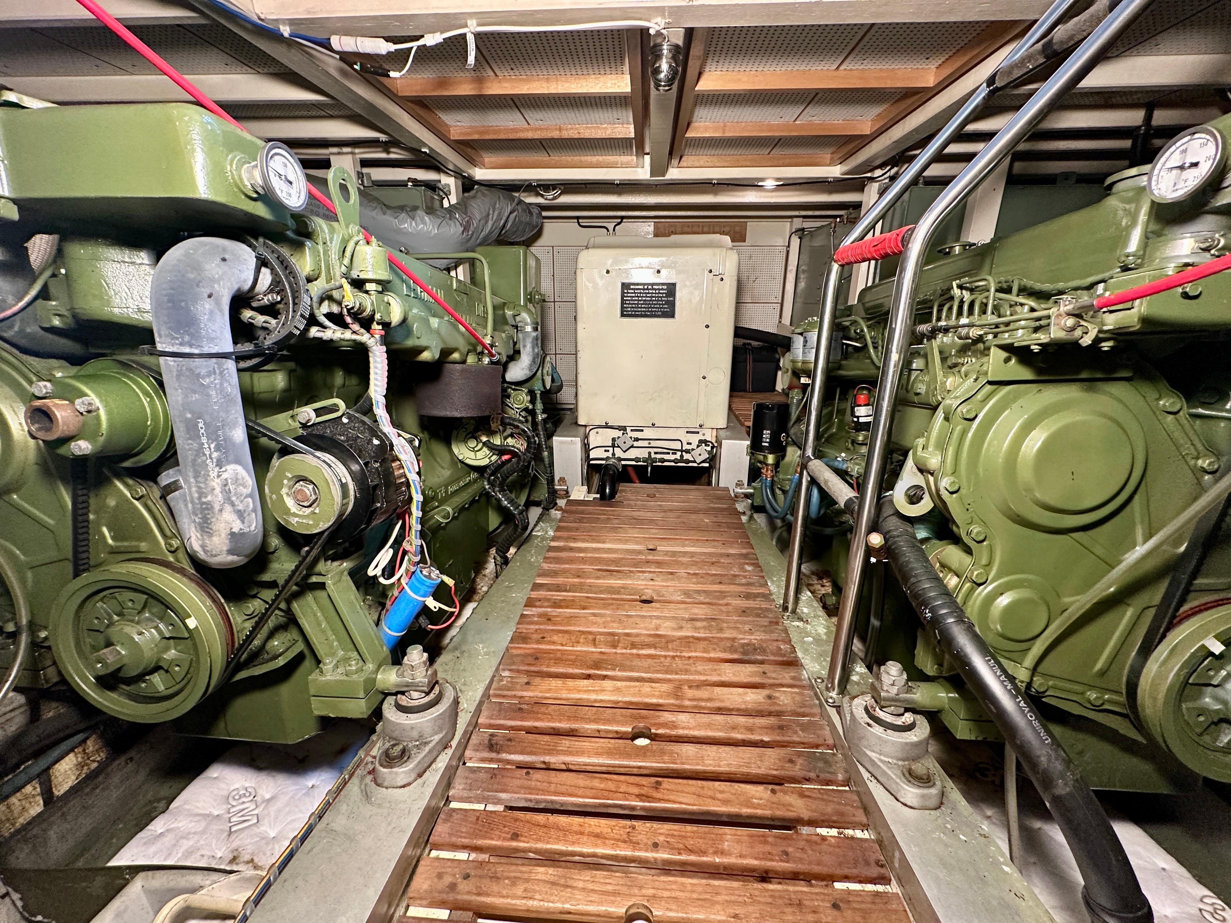 Engine room of 1982 Grand Banks Classic boat with dual green engines and wooden walkway.