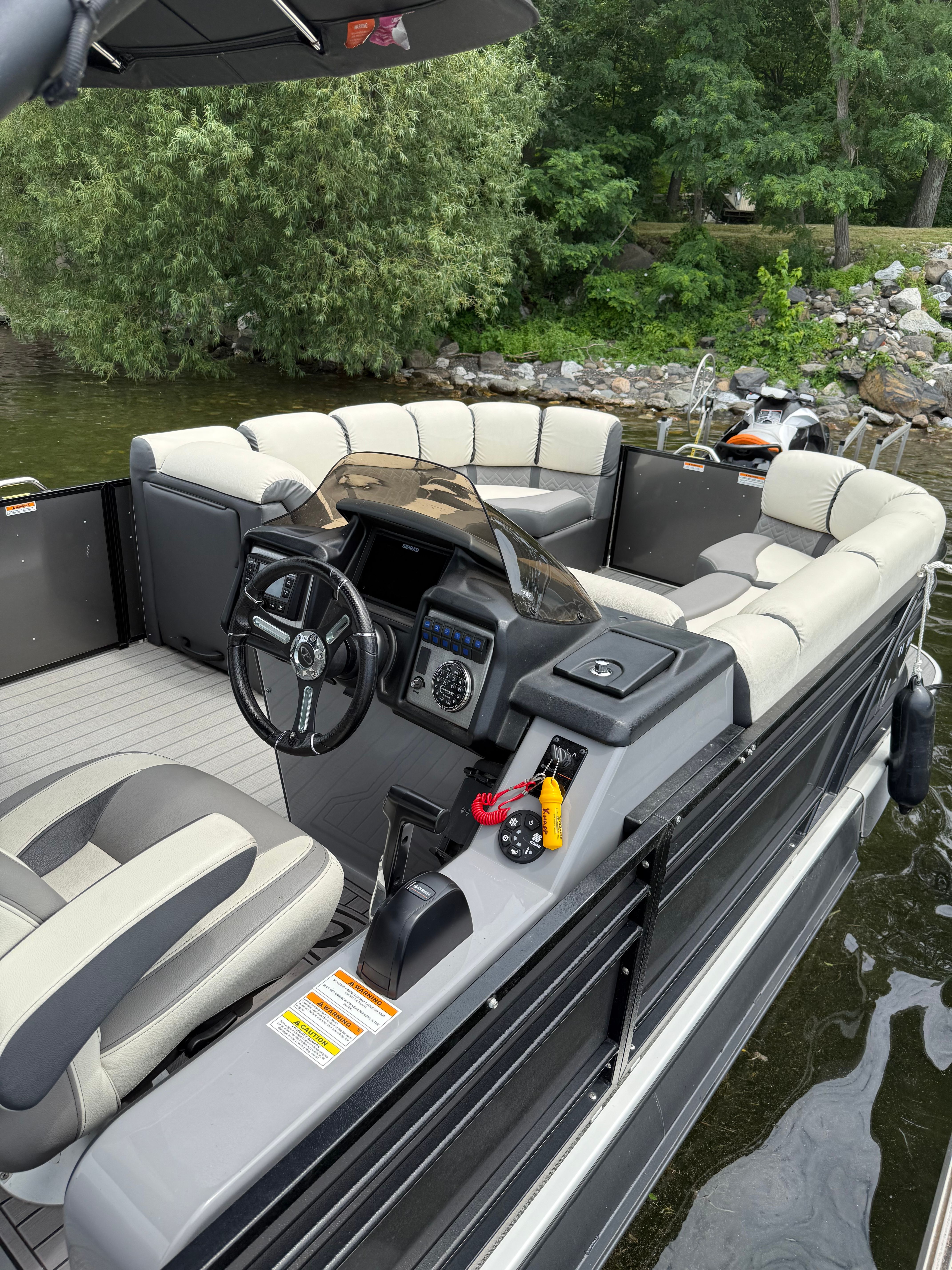 The image shows a modern pontoon boat with comfortable seating and a sleek helm station.