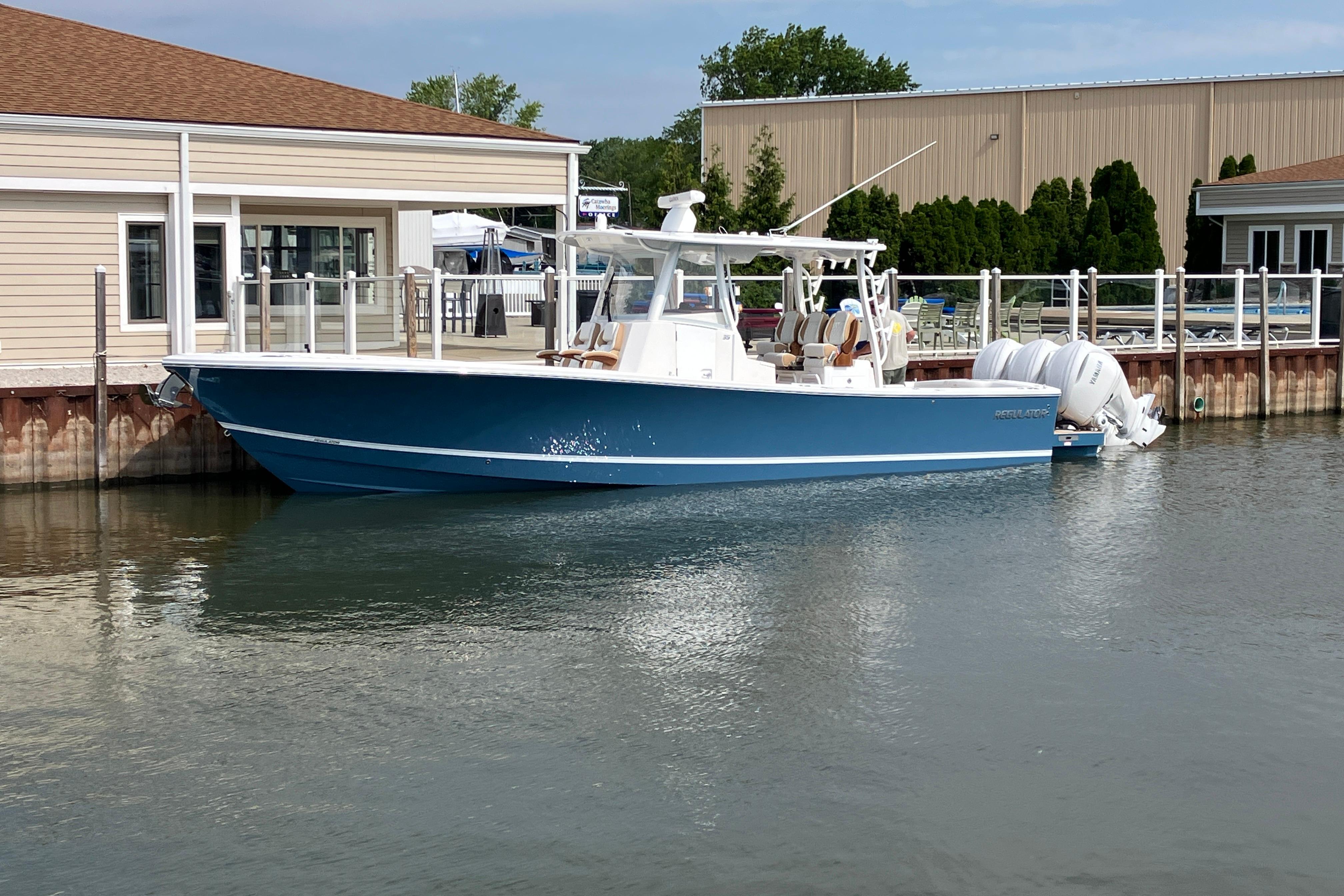 2027 Regulator 35 boat docked by a waterfront building, featuring sleek blue design.