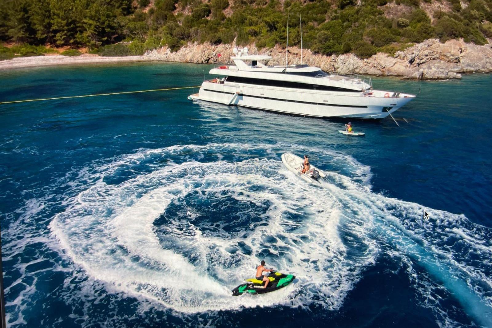 Luxurious 1991 Crestitalia 33m yacht anchored near scenic coastline with jet skis and boats.