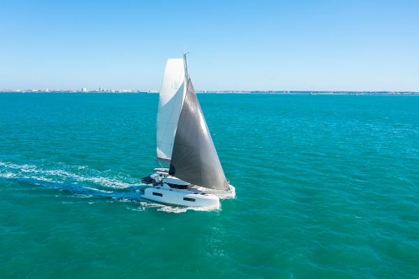 2025 Lagoon 38 sailing catamaran gliding on turquoise ocean waters under clear blue sky.