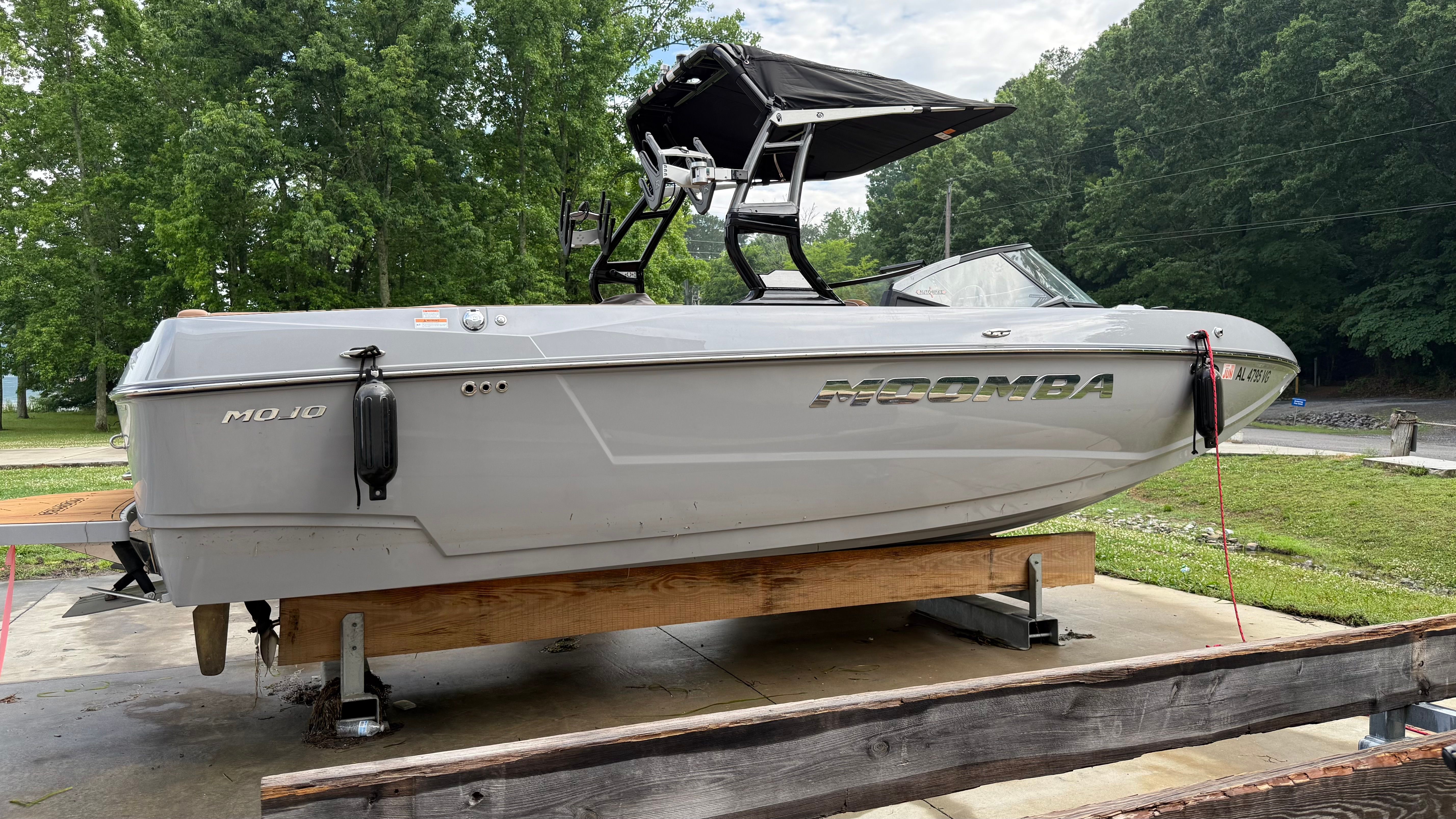 A gray motorboat on a wooden stand outdoors, surrounded by trees.