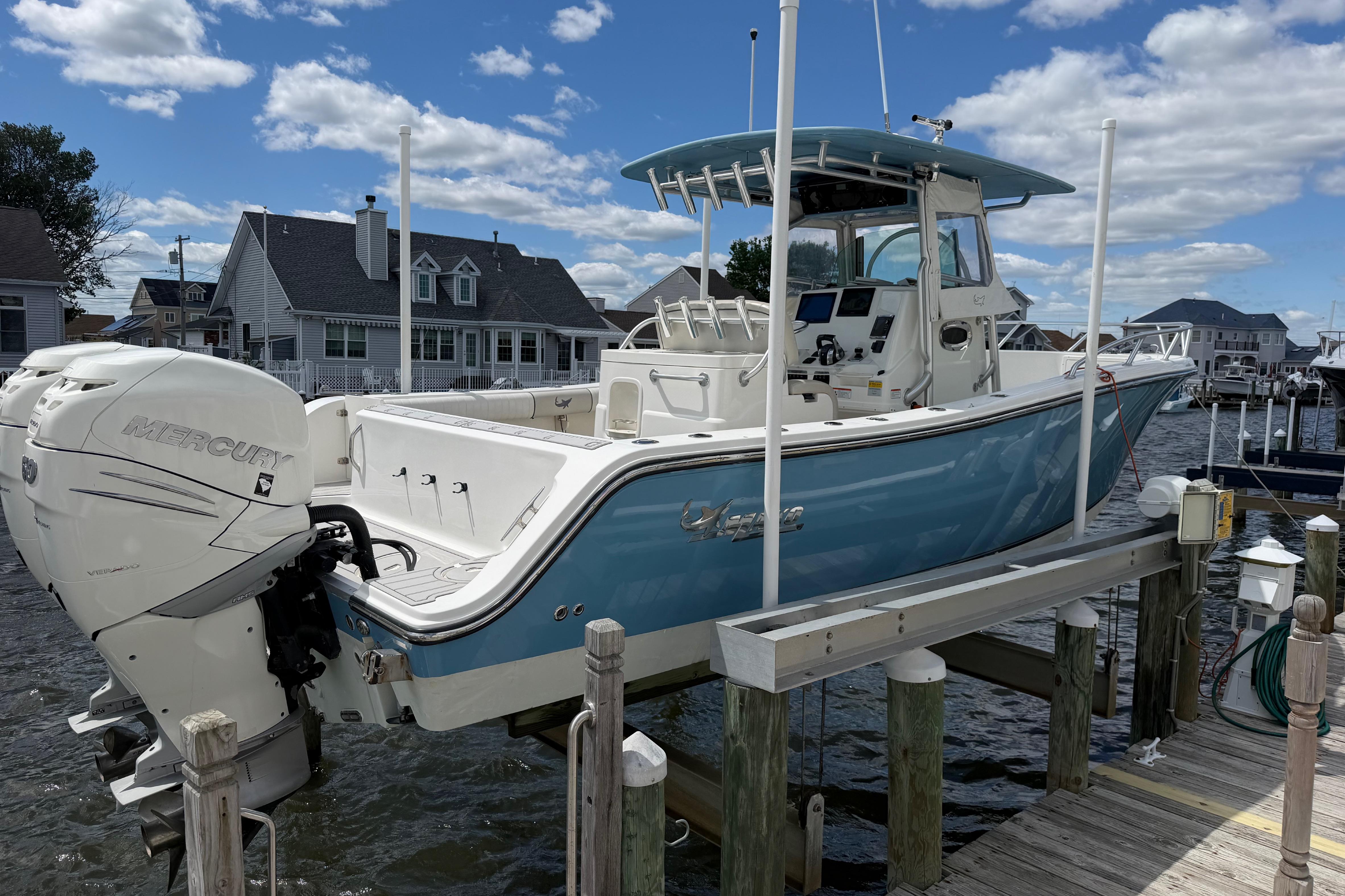 2017 Mako 284 Center Console boat on lift, featuring Mercury outboard engine, docked by waterfront homes.