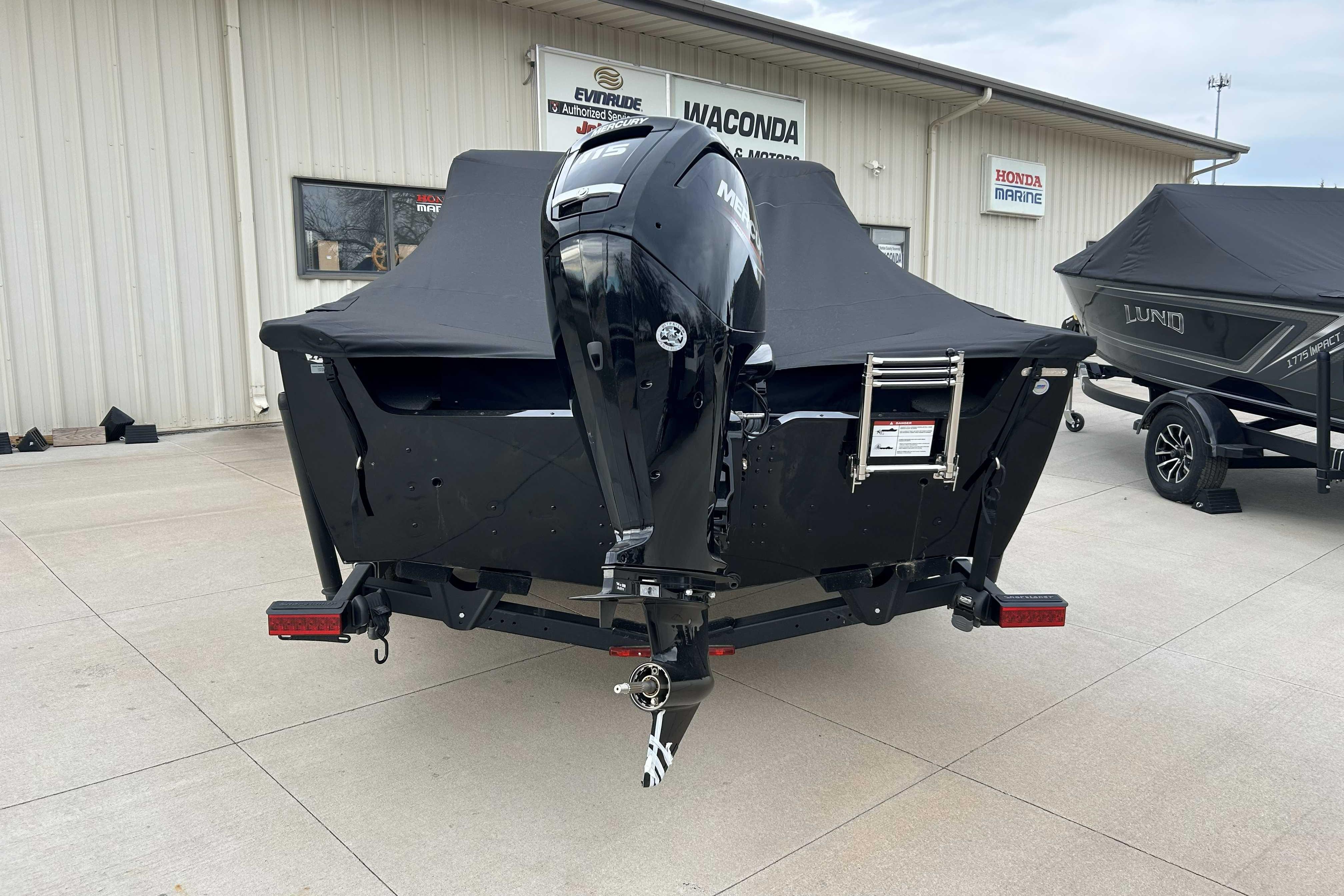2026 Lund 1800 Explorer Sport boat with outboard motor, covered and parked outside dealership.