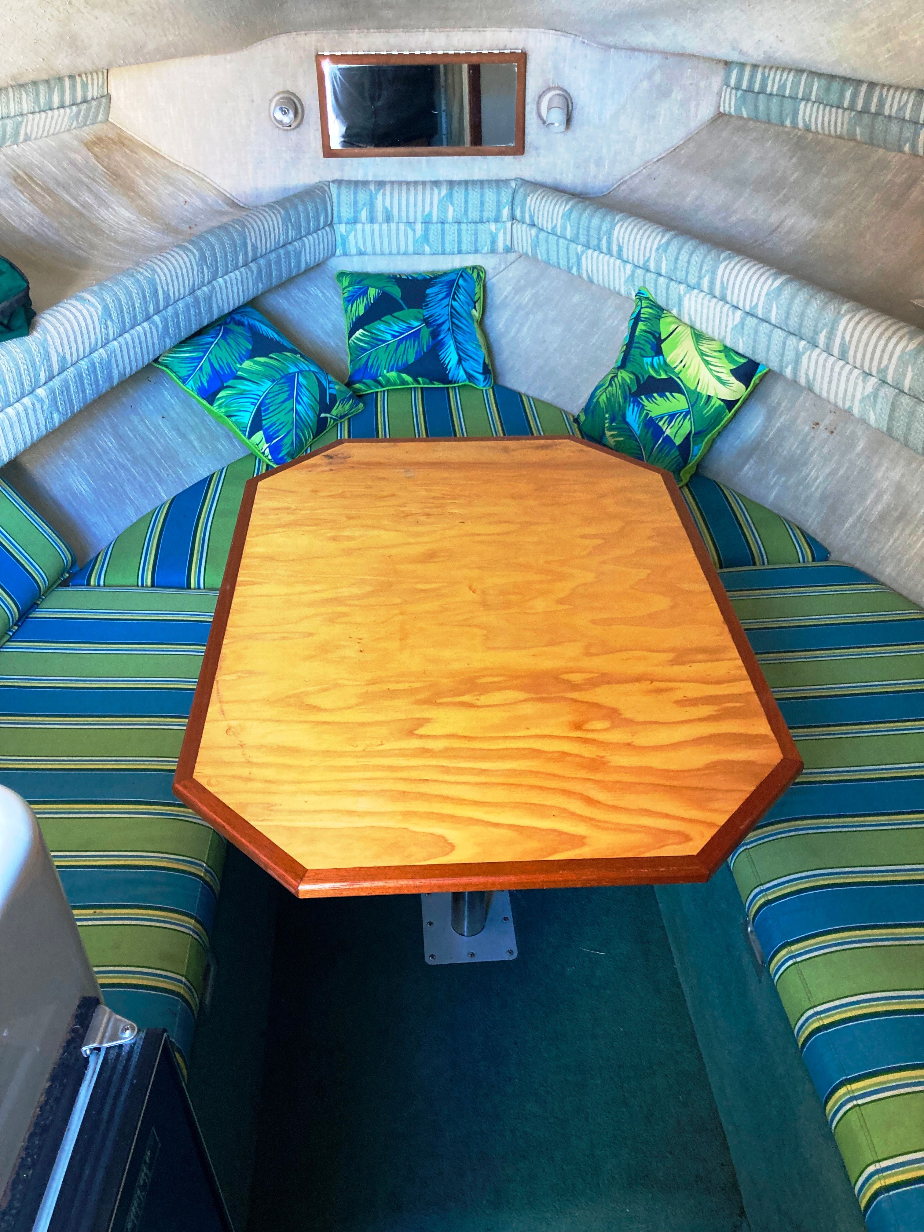 Interior of a 1991 Sea Ray 220 Sundancer with a wooden table and colorful cushions.