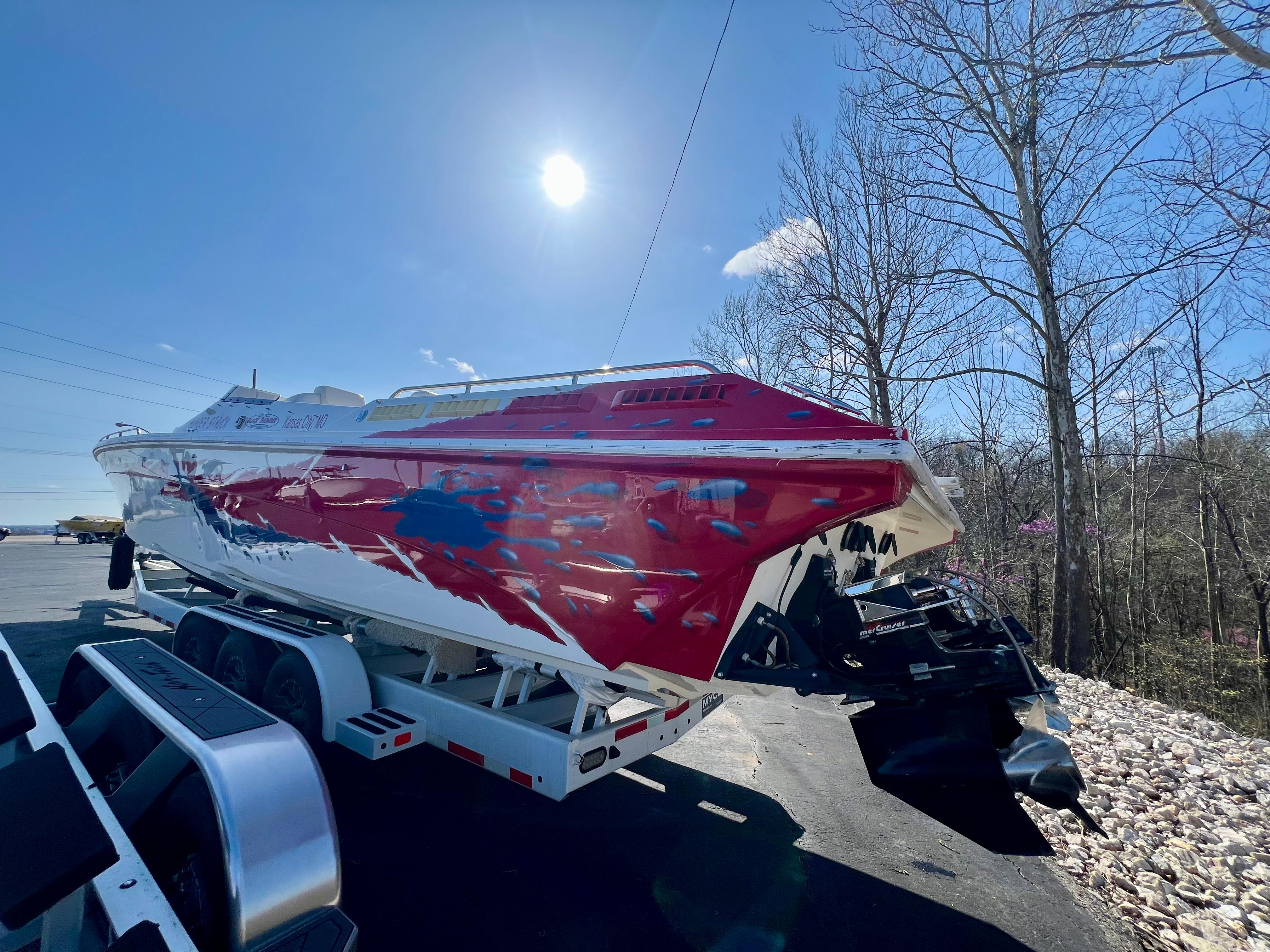 1999 Black Thunder 430 Flat Deck boat on trailer under bright sun, surrounded by trees.