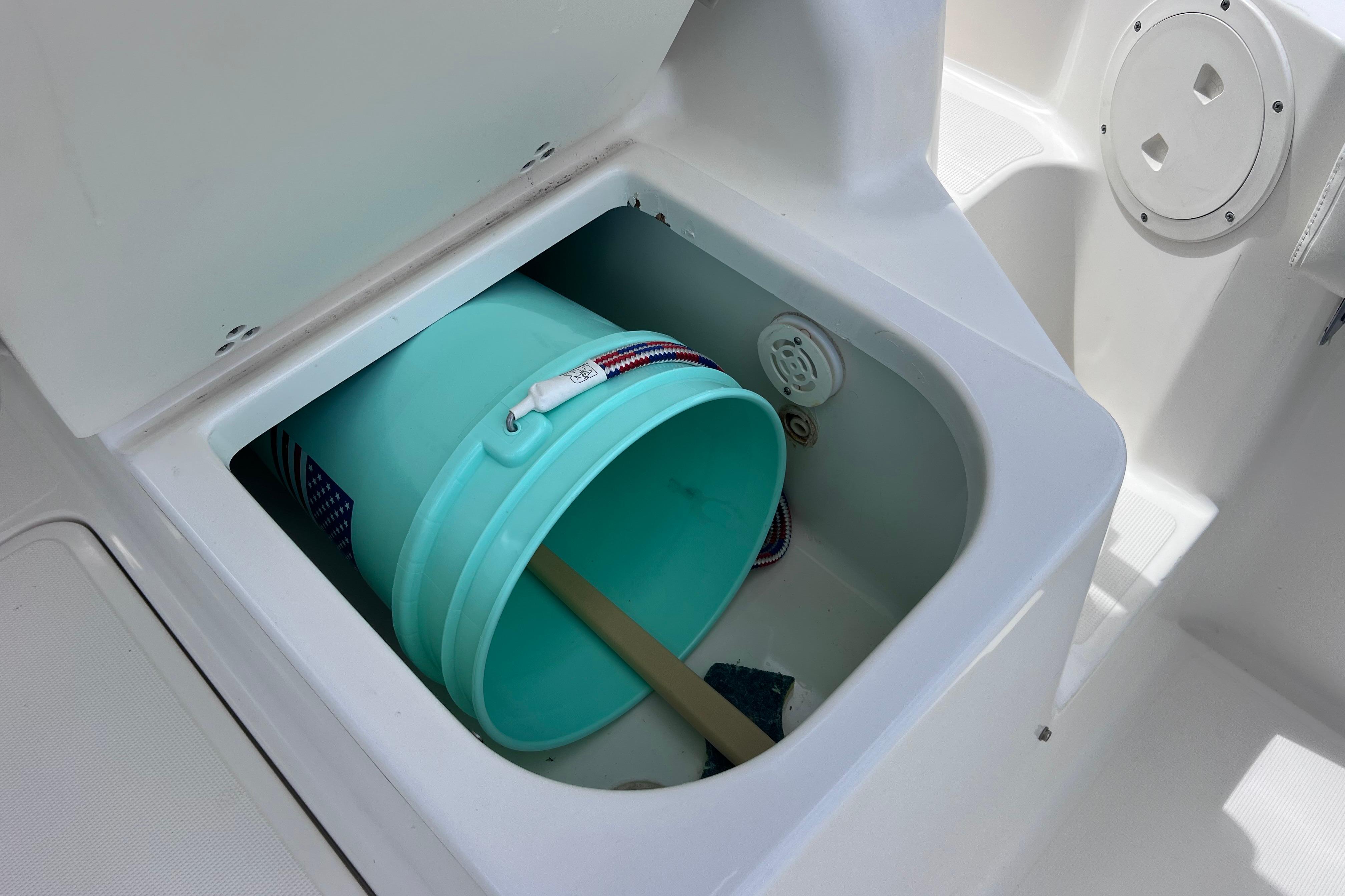 Storage compartment on a 2004 Pursuit 2870 Walkaround boat with a turquoise bucket inside.