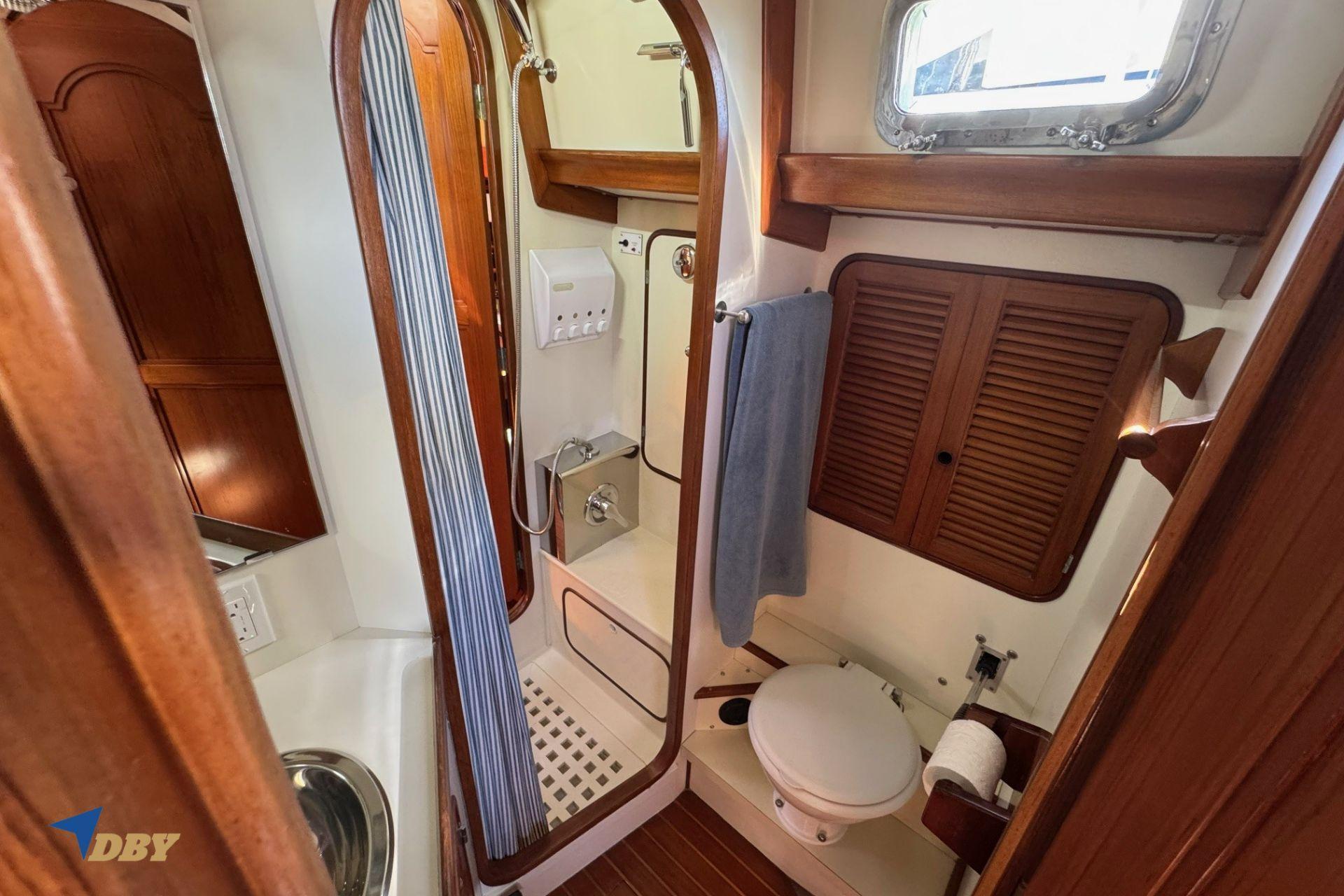 1983 Mason 53 yacht bathroom with wooden accents, shower, and porthole window.
