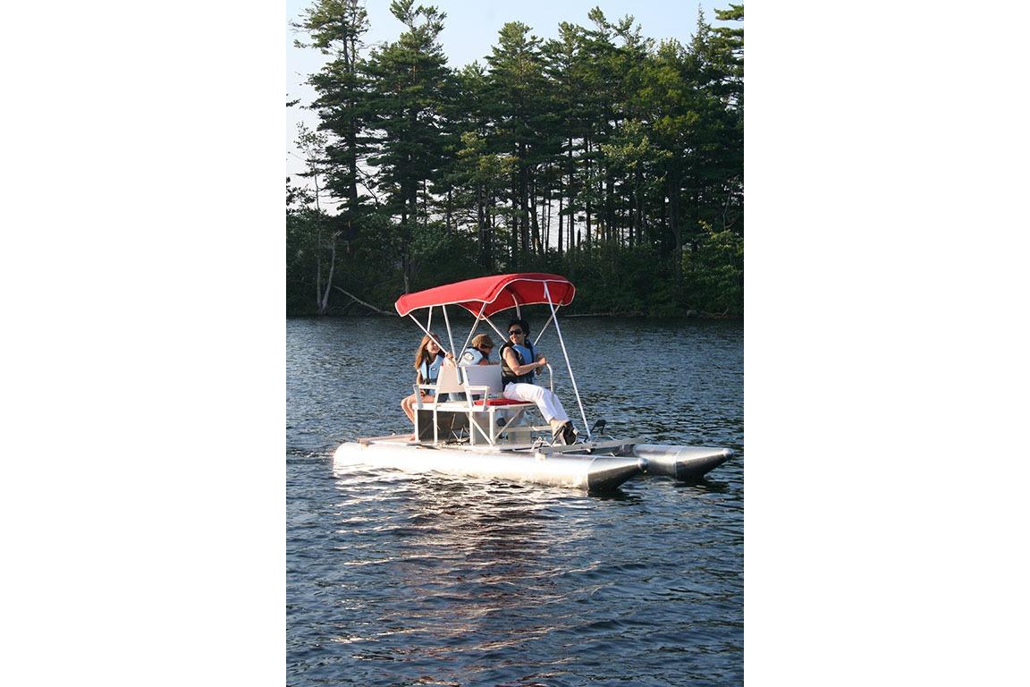 People enjoying a ride on a 2026 Aqua Cycle 2 pedal boat with a red canopy.