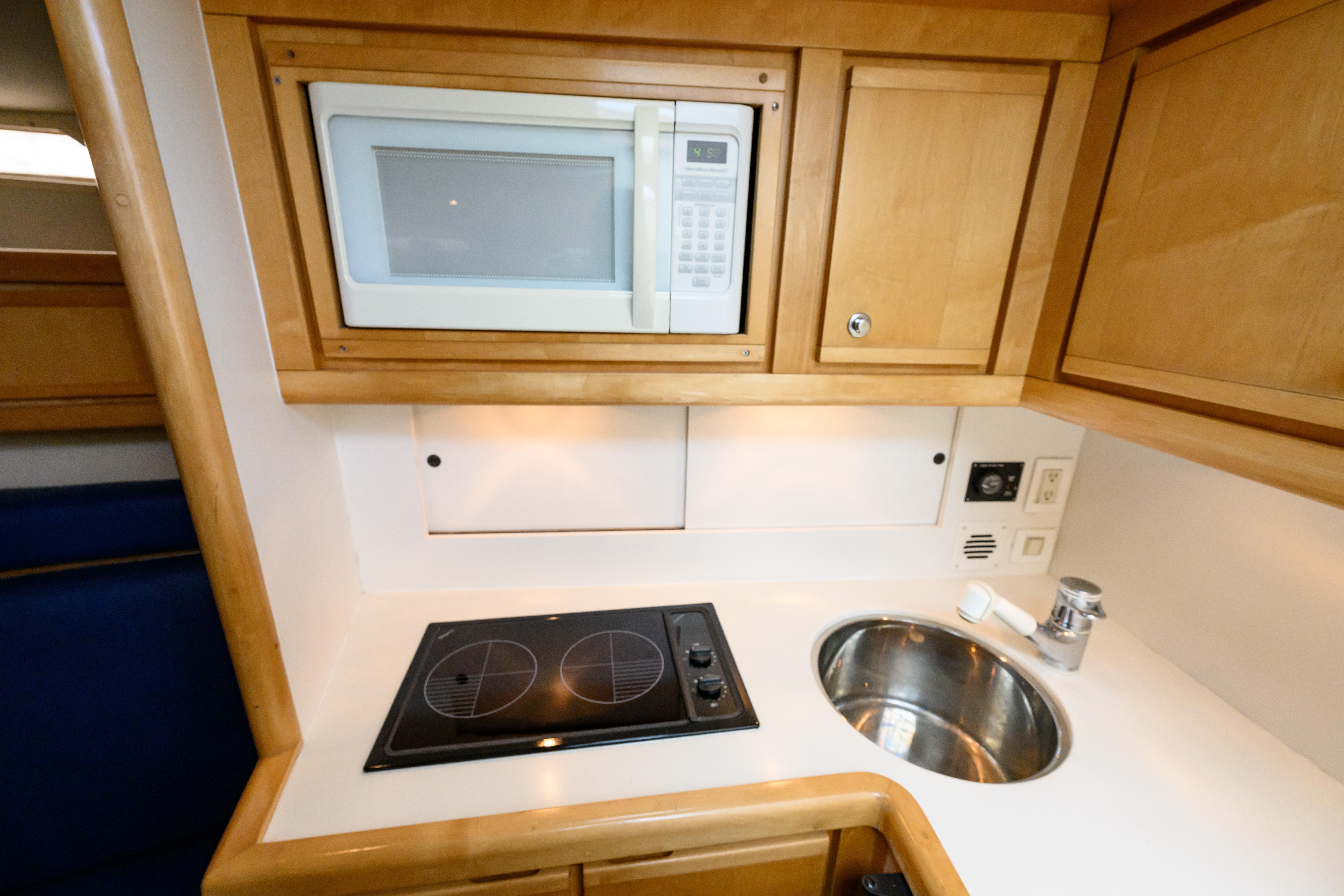 Compact kitchen area in a 1998 Bertram 36 Moppie yacht with microwave and stovetop.